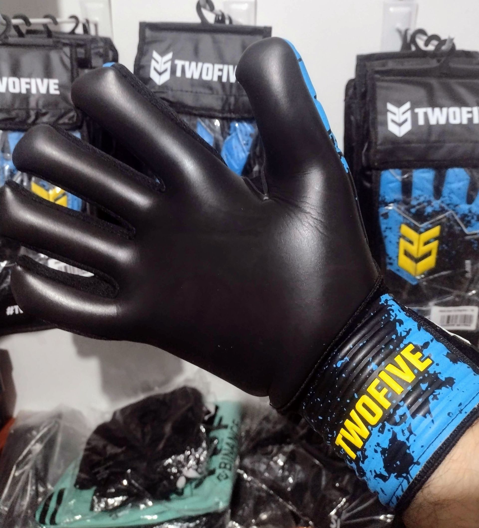 Guante de boxeo negro con muñequera azul y amarilla, sostenido en interiores con el empaque del guante al fondo.
