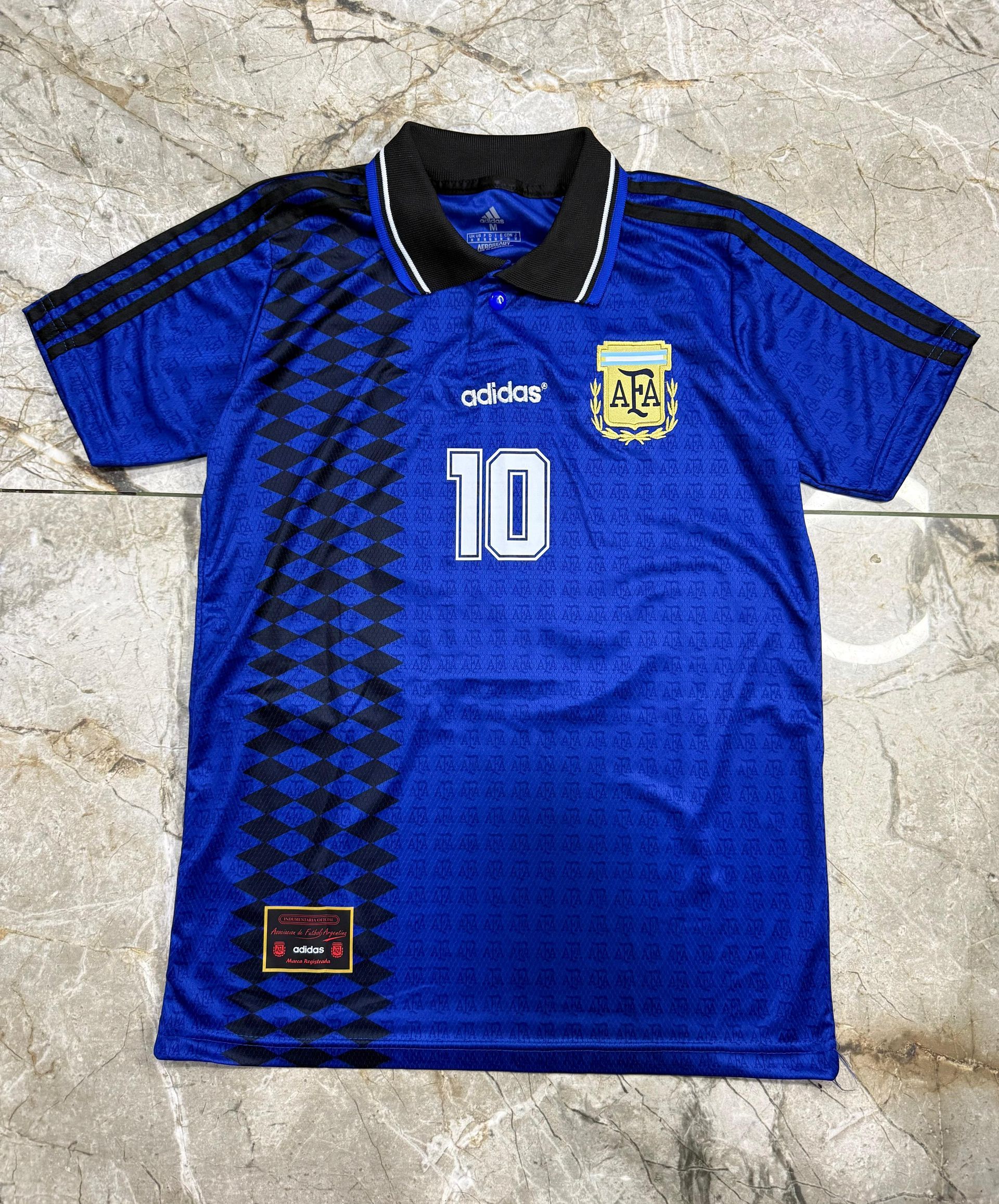 Una camiseta azul de la selección argentina de fútbol con el número 10, cuello negro y una franja vertical negra estampada.
