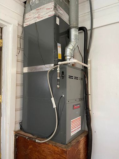 Gray furnace with ductwork in a narrow utility closet beside a brick base and white walls