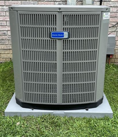 Outdoor HVAC unit with gray grille panels on a concrete pad against a brick wall.