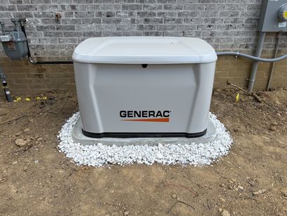 Generac standby generator on white gravel beside a brick wall outdoors