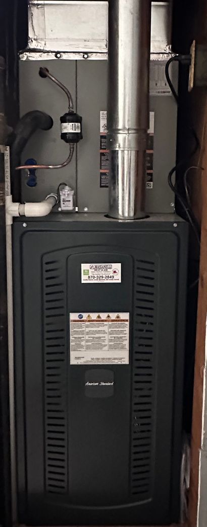 Basement furnace with dark front panel, silver vent pipes, and surrounding utility lines.