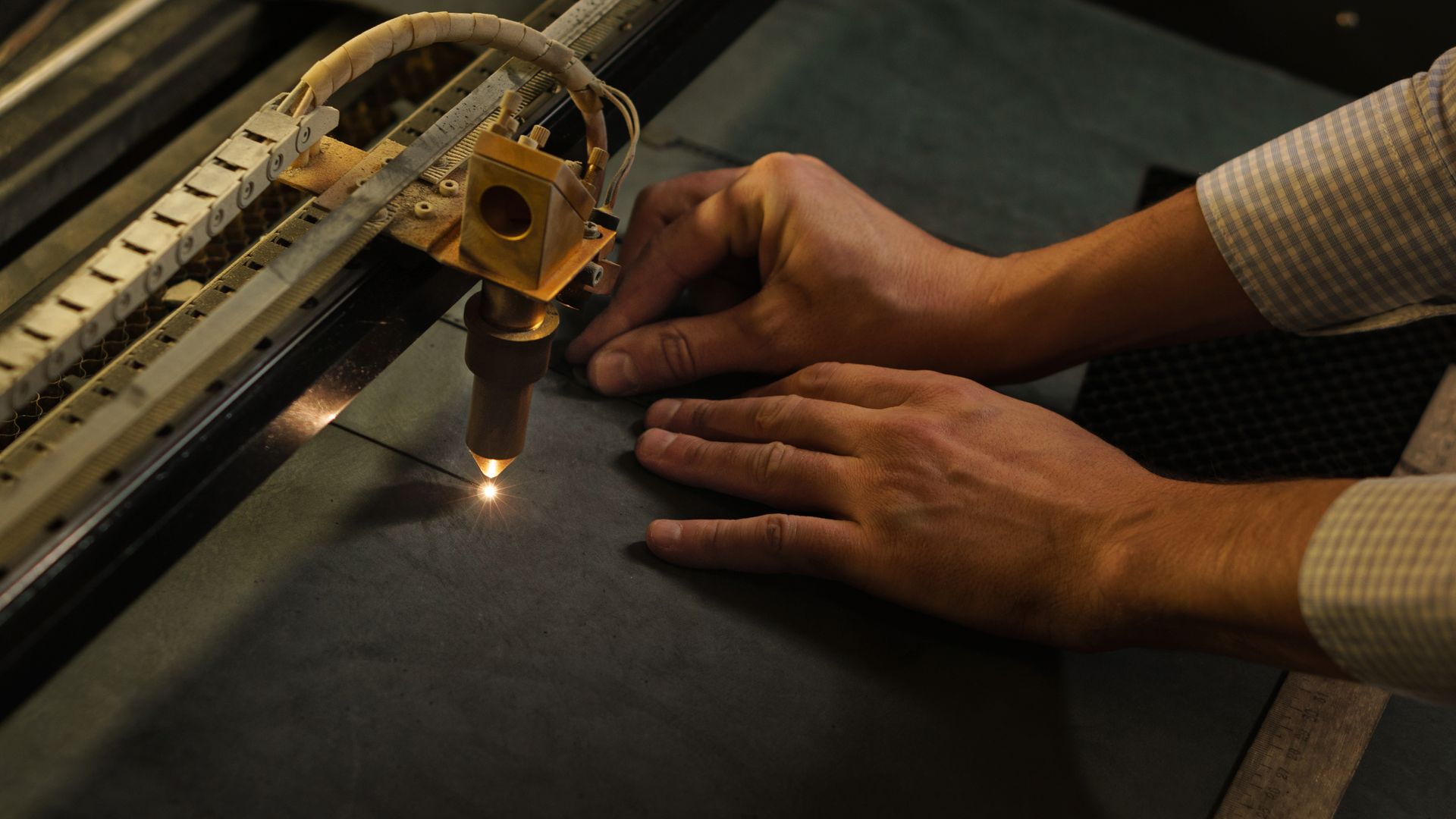 Laser Cutter Cutting a Dark Material With Hands Guiding the Process — Bryants Laser Works in Ipswich, QLD
