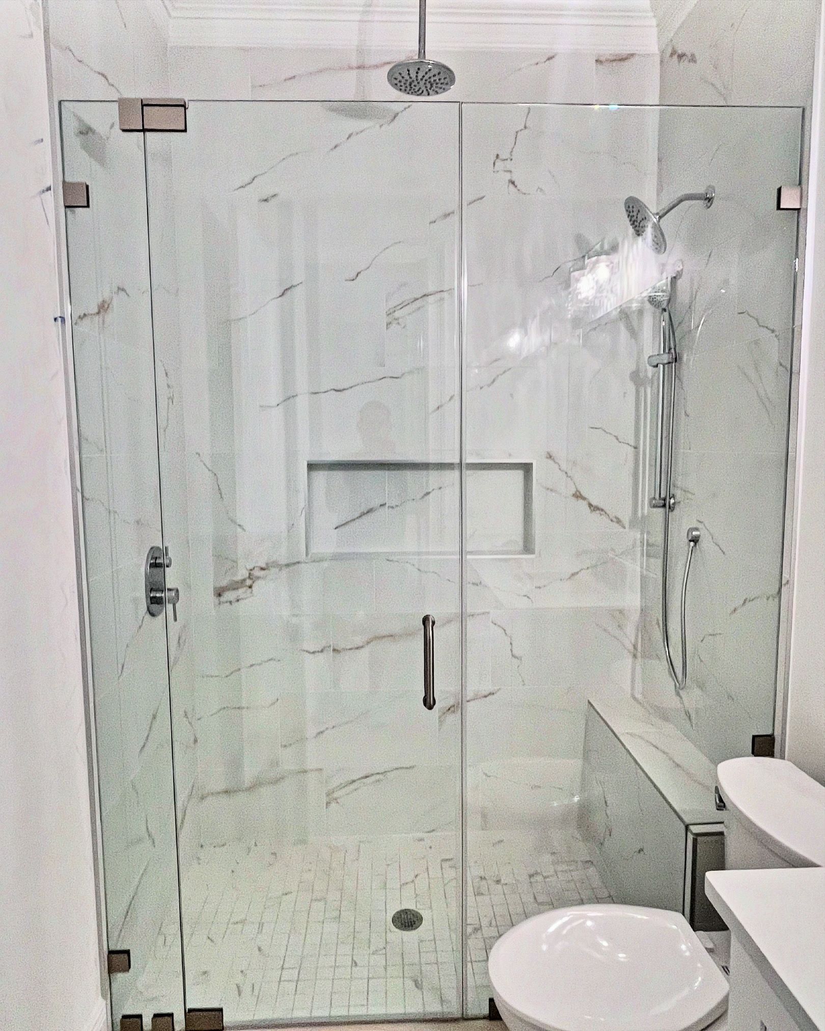 Glass shower enclosure with marble tile walls, showerhead, and a toilet.