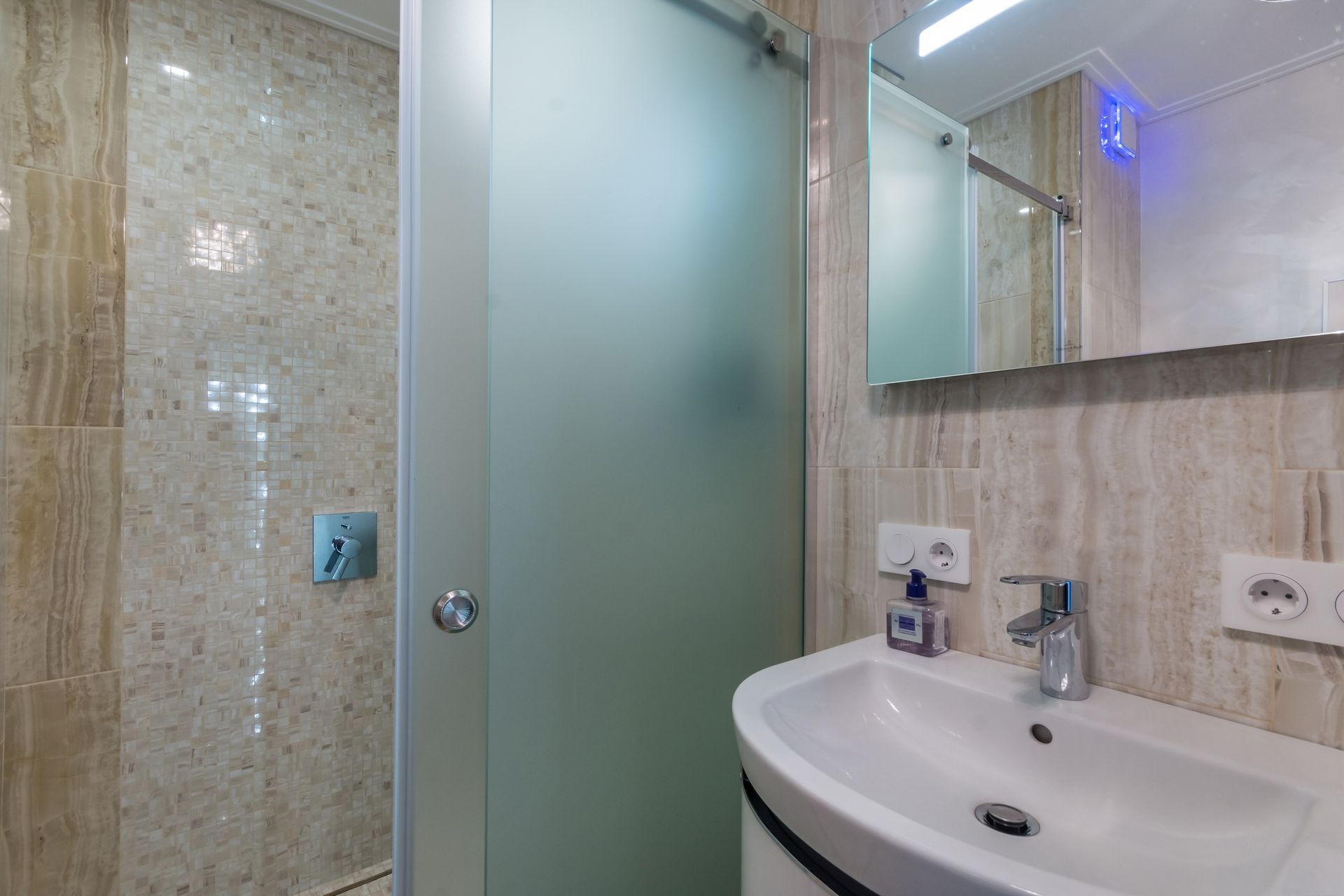 Bathroom with a white sink, frosted glass shower door, and beige tiled walls.