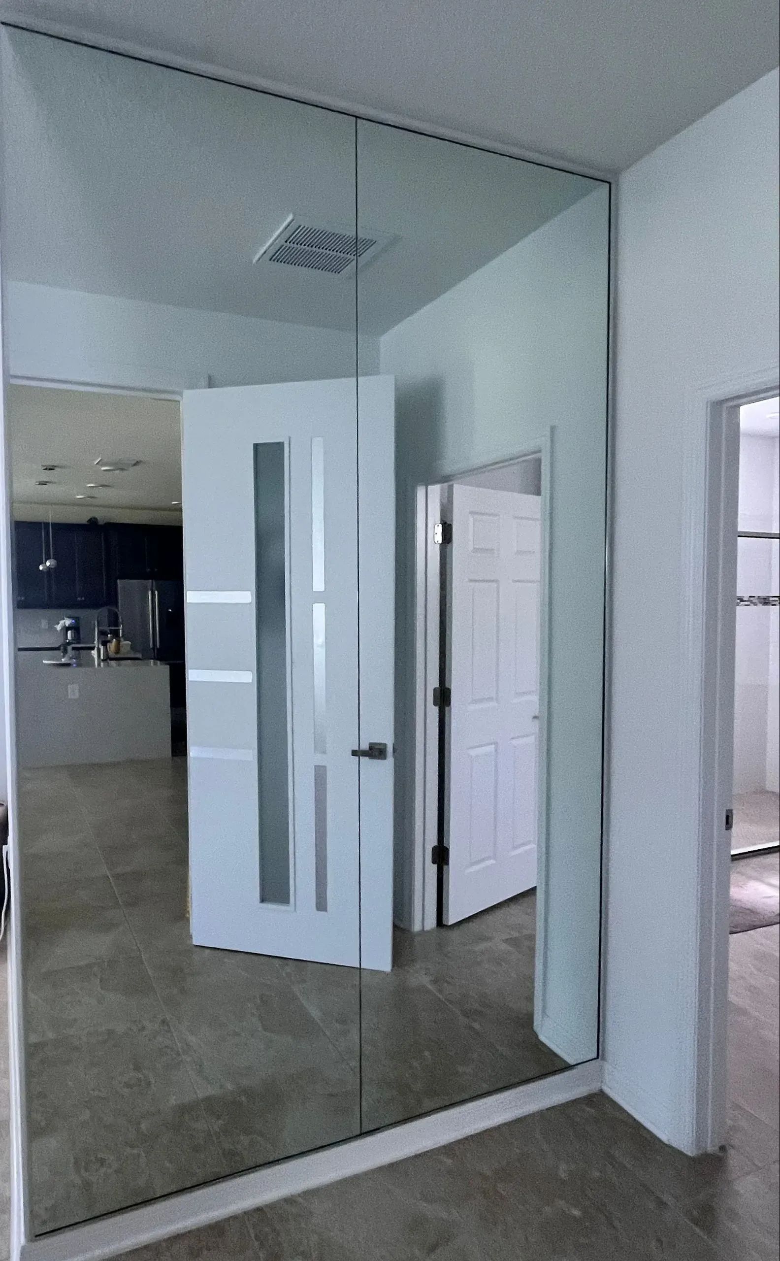 Room with mirrored wall, white doors, and a glimpse of a kitchen.