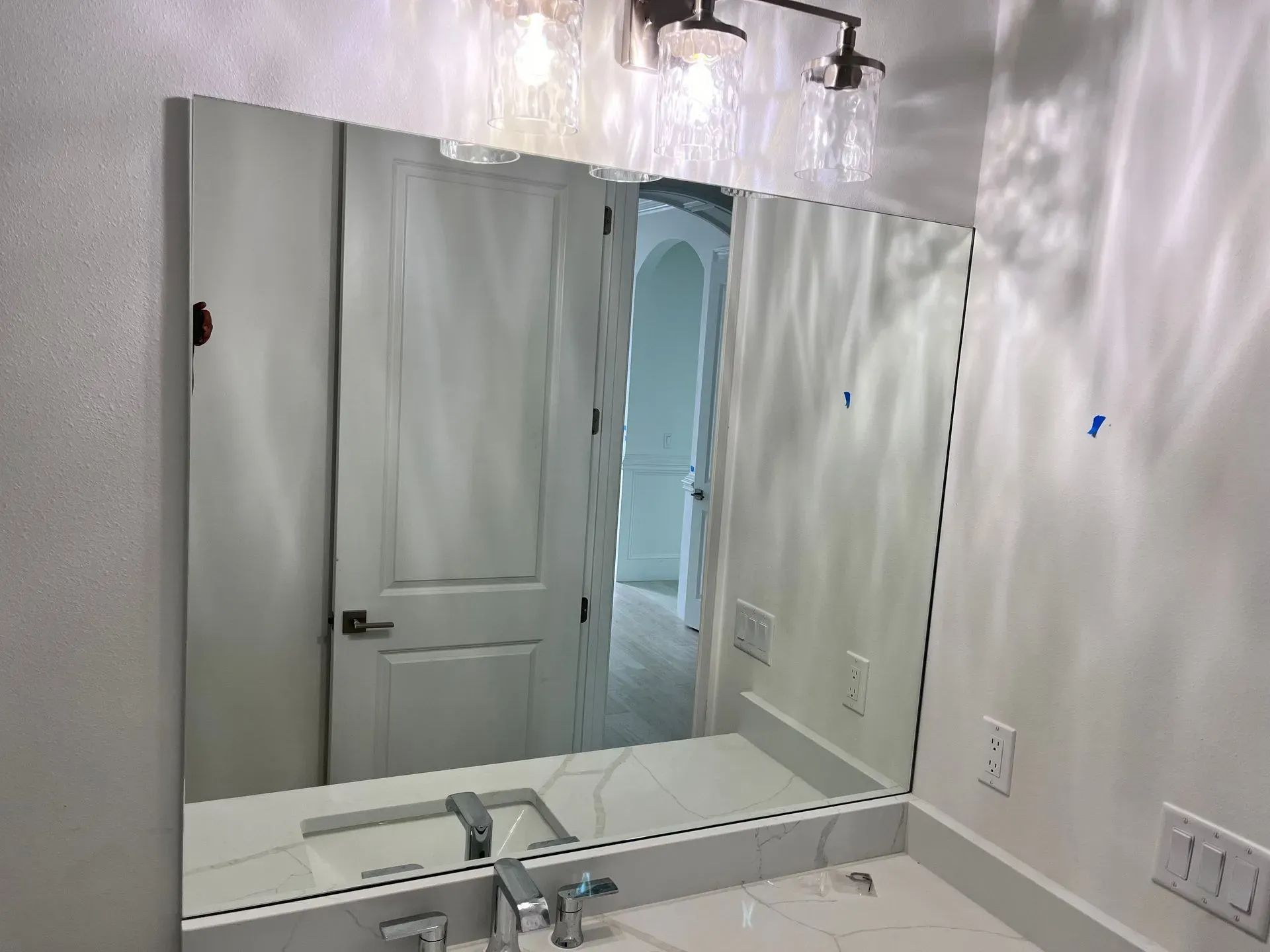 Bathroom mirror over sink reflects door and light fixtures.