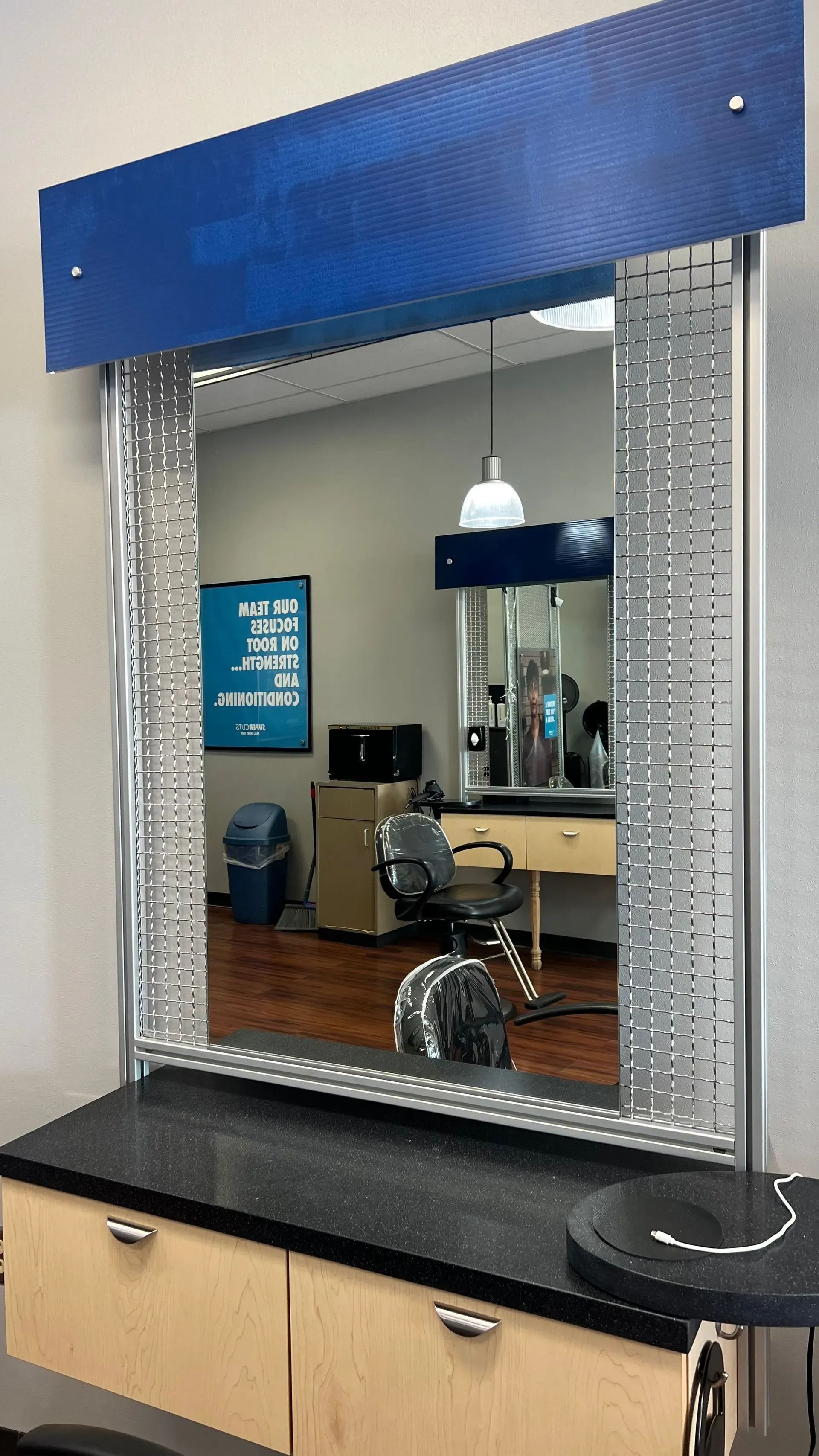 Salon mirror with a blue top. The mirror is above a black countertop with a cabinet.
