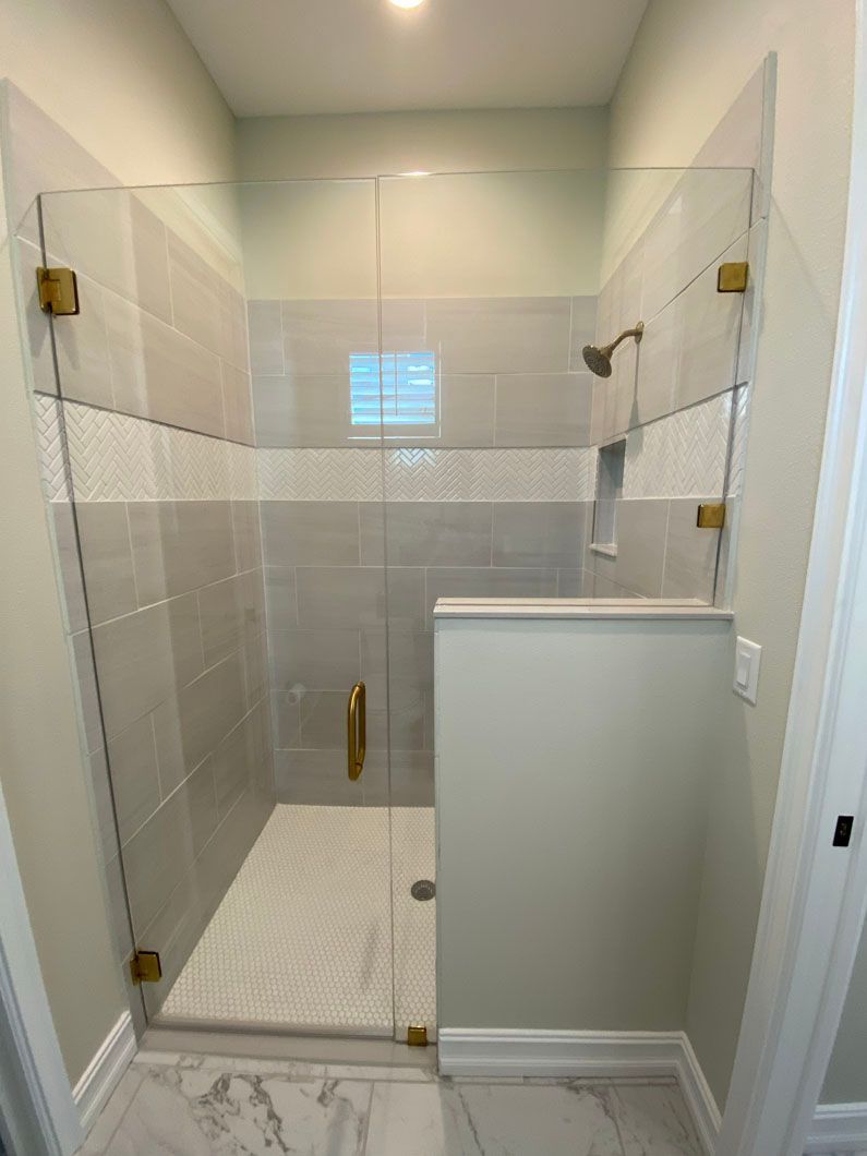 Glass shower enclosure with gold hardware, tiled walls, and white floor.