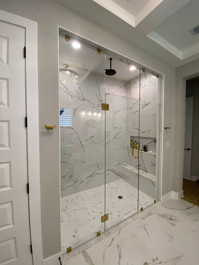 Glass shower enclosure with gold hardware, white marble tile, and a black showerhead.