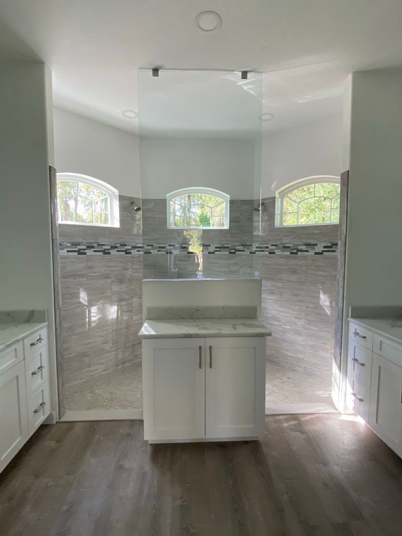 Bathroom with center vanity, shower, and arched windows. White cabinets, tile walls, and wood-look flooring.