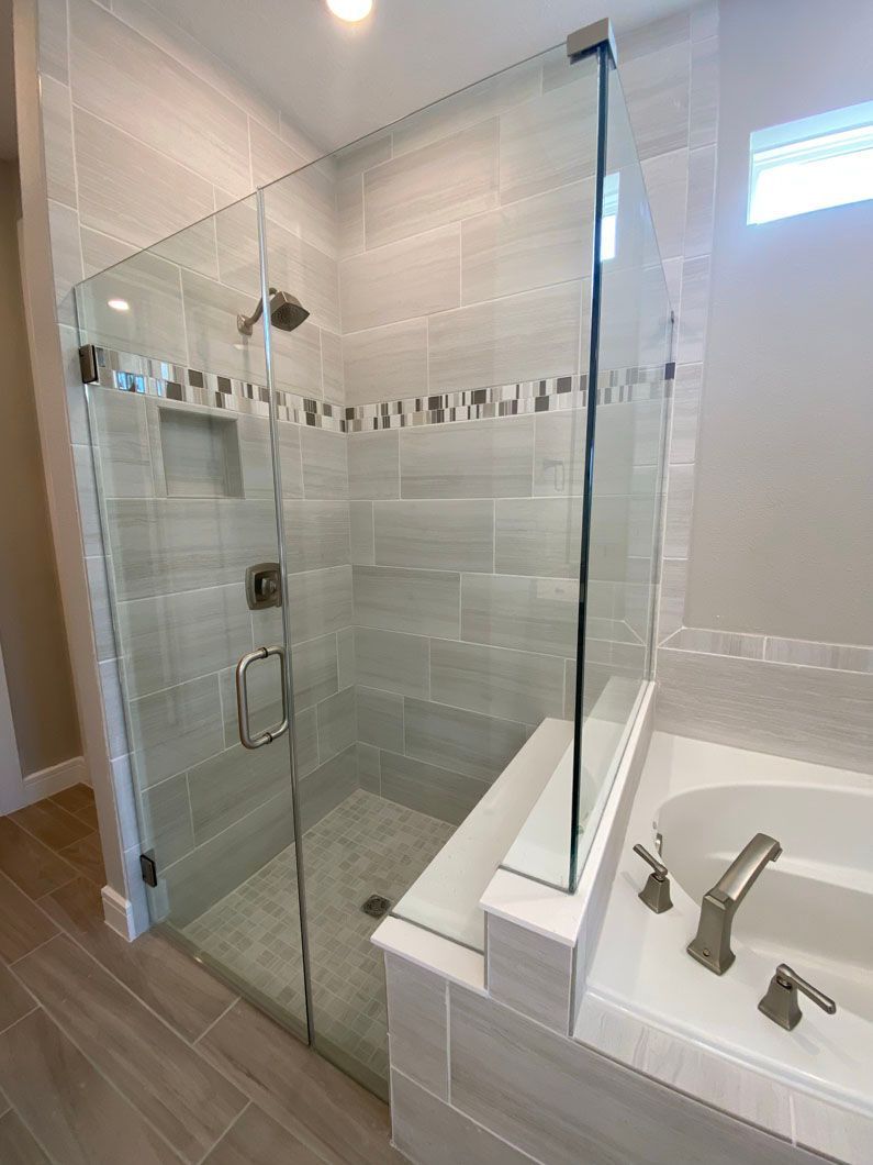 Glass-enclosed shower with tiled walls and a built-in bench, adjacent to a bathtub.
