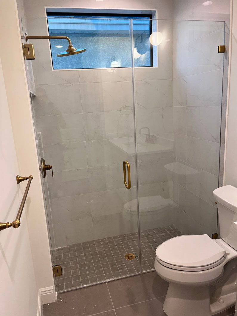 A modern bathroom with a glass shower enclosure and gold fixtures. The toilet is to the right.