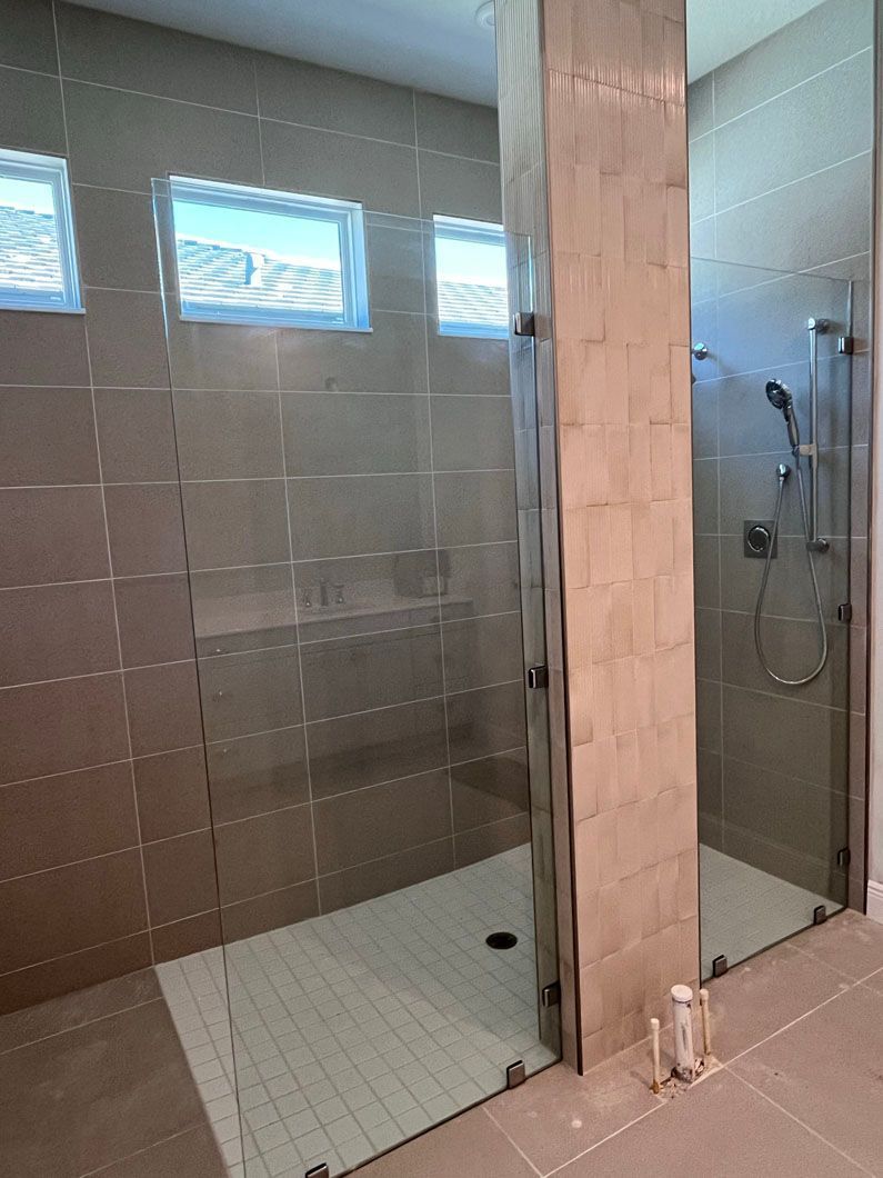 Modern bathroom with glass shower enclosure, beige tiled walls, and small windows.