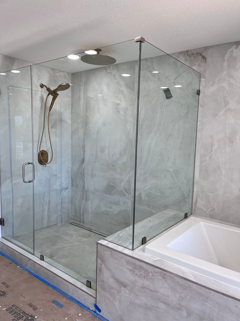 Glass shower enclosure in a bathroom with a marble-effect wall and a built-in bathtub.