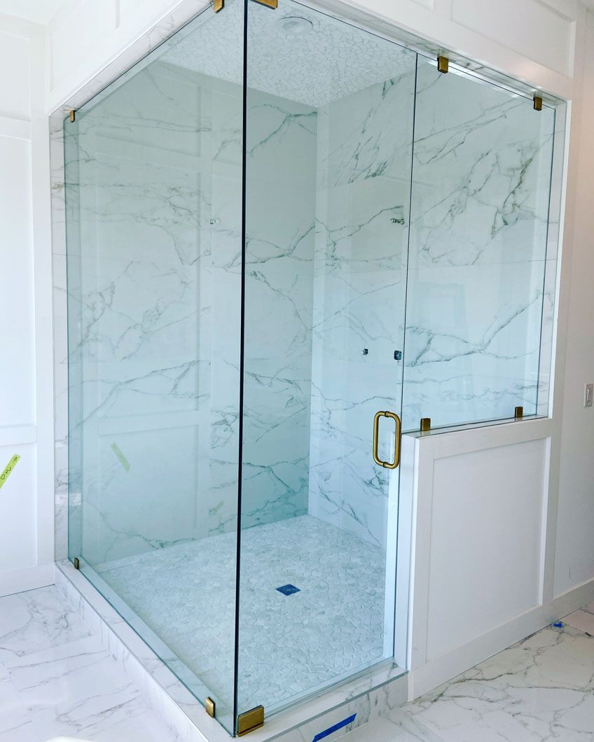 Glass shower enclosure with gold hardware and white marble tile.