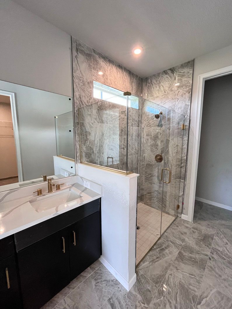 Modern bathroom with a glass shower, marble tile, and black vanity.