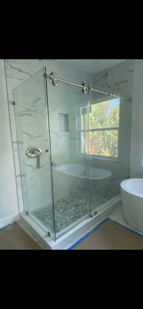 A modern glass shower enclosure with marble tile walls and a pebble-stone floor in a bathroom.