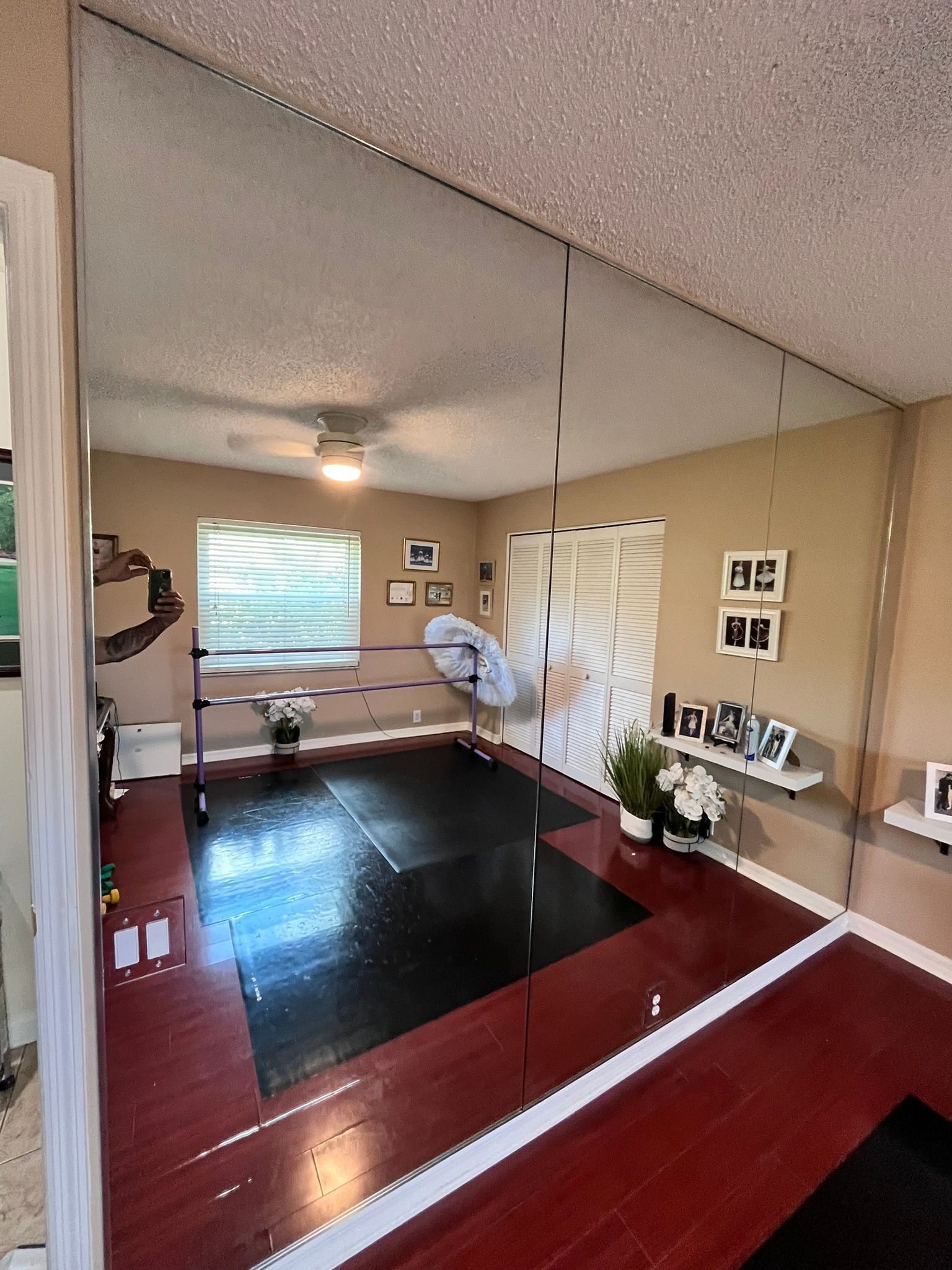 Dance studio with mirrored wall, barre, dark floor, and red wood floor.