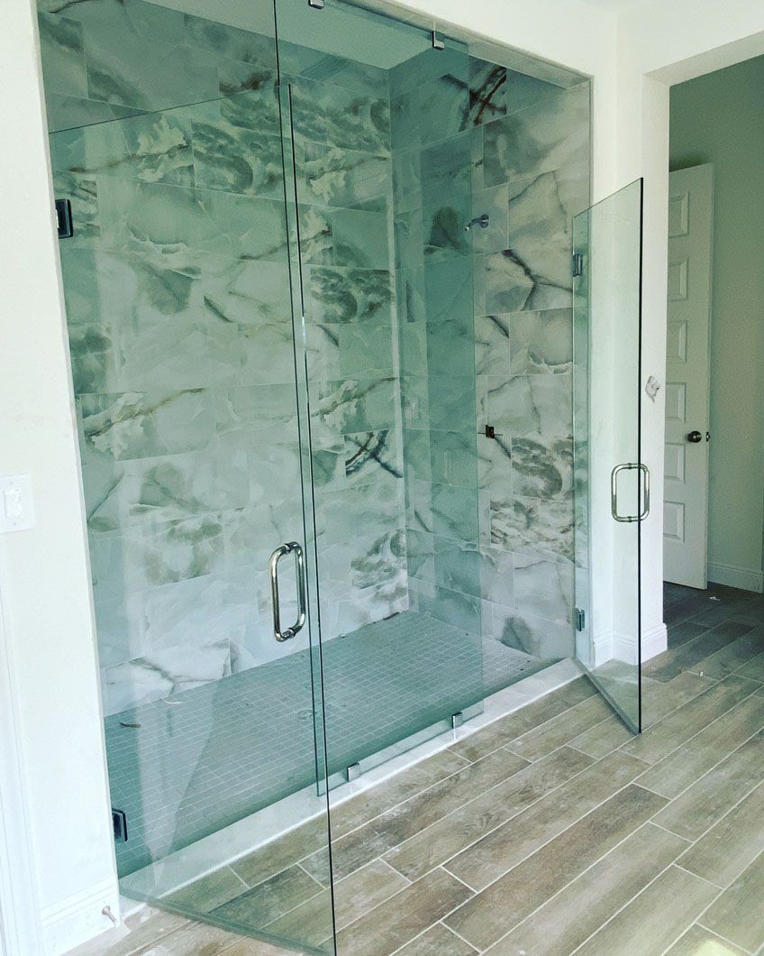 Glass shower enclosure with marble tile, open door, light wood floor.