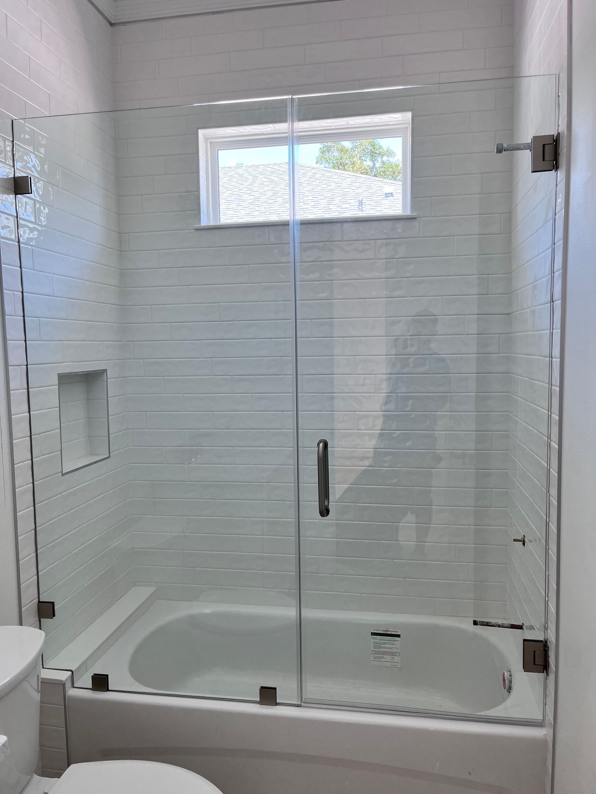 Glass shower enclosure with white tile walls and a small window.