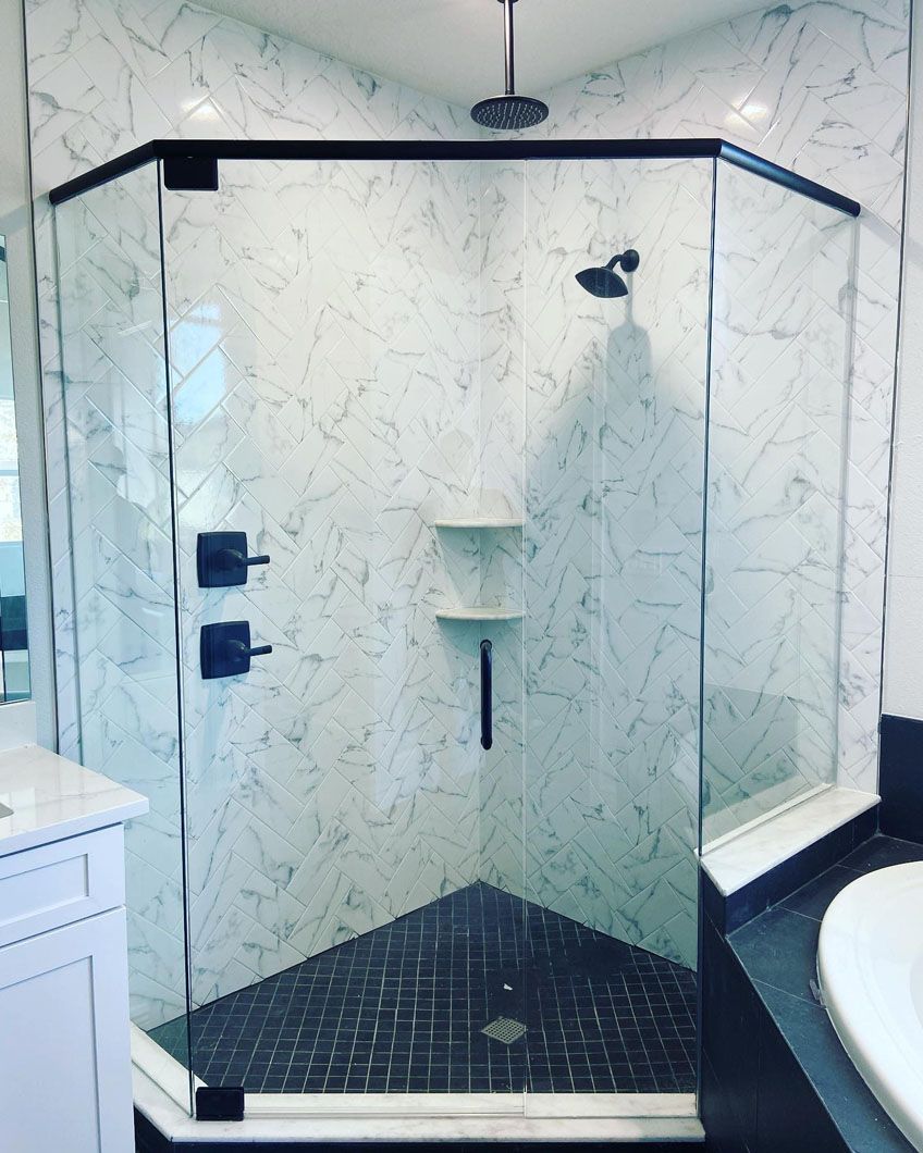 Corner shower with marble-like tile walls, black fixtures, and glass enclosure.
