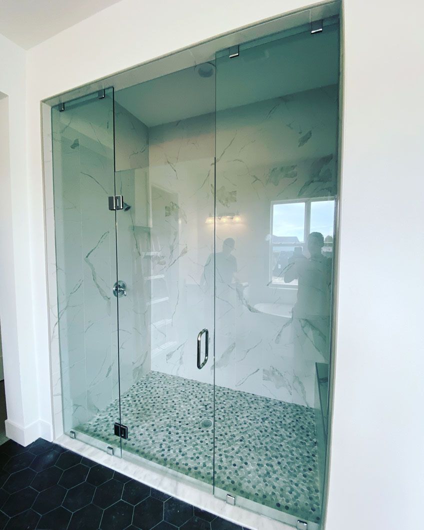 Glass-enclosed shower with marble-patterned walls and pebble floor