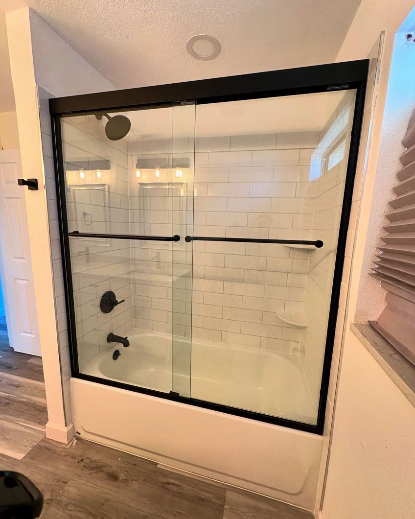 Shower with black frame and sliding glass doors, white tub, and tile.