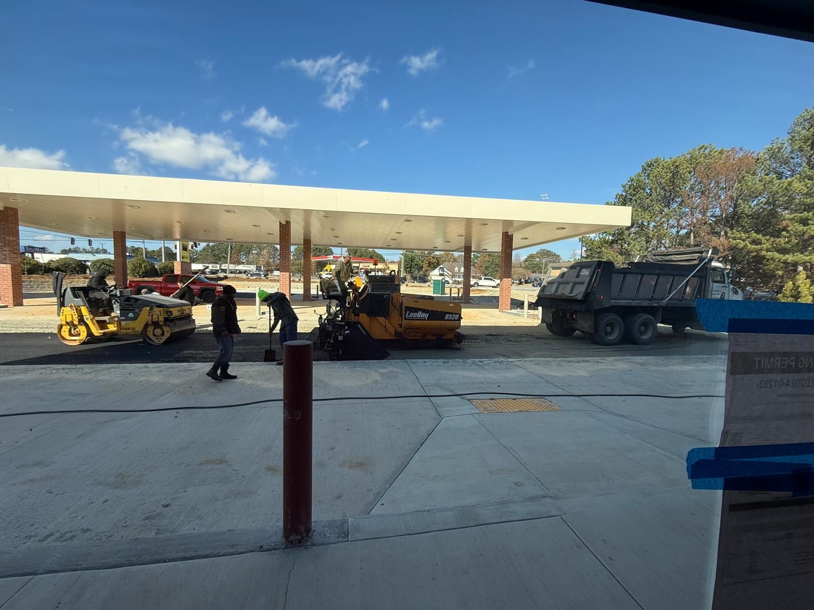 Commercial asphalt paving crew with LeeBoy paver and roller compactor installing parking lot under fuel canopy in Marietta Georgia