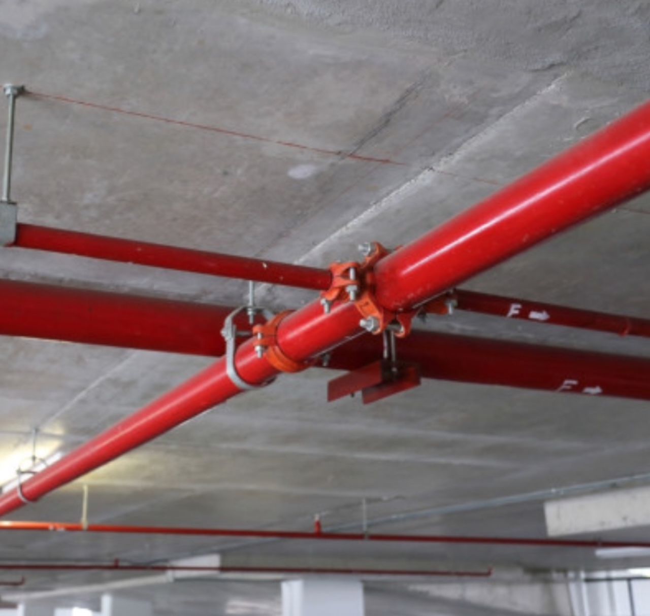 Commercial fire suppression system with red pipes and orange grooved mechanical couplings at concrete ceiling in Roswell Georgia