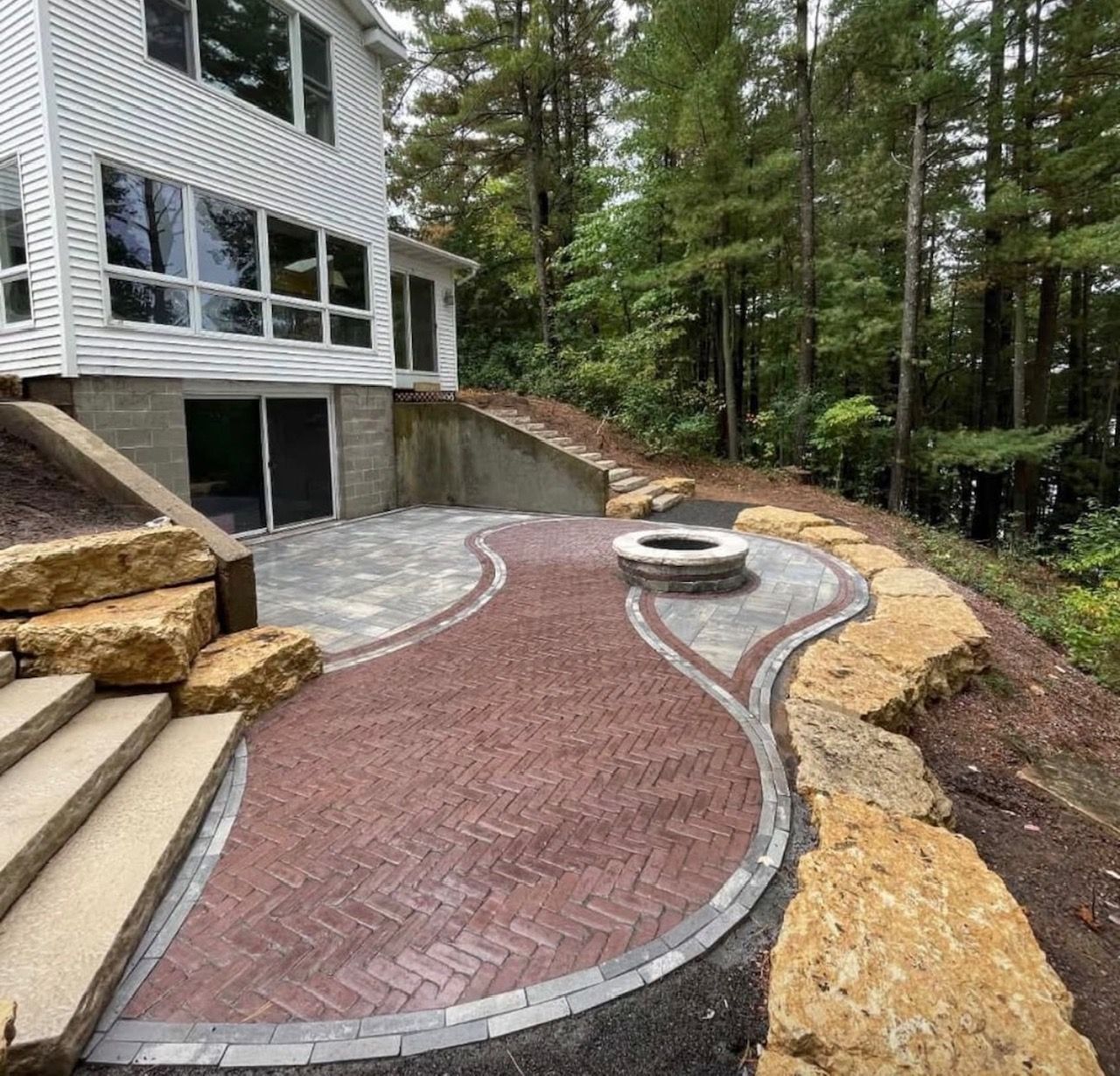 Luxury herringbone paver patio with fire pit, curved border, and natural boulder retaining walls in Marietta Georgia