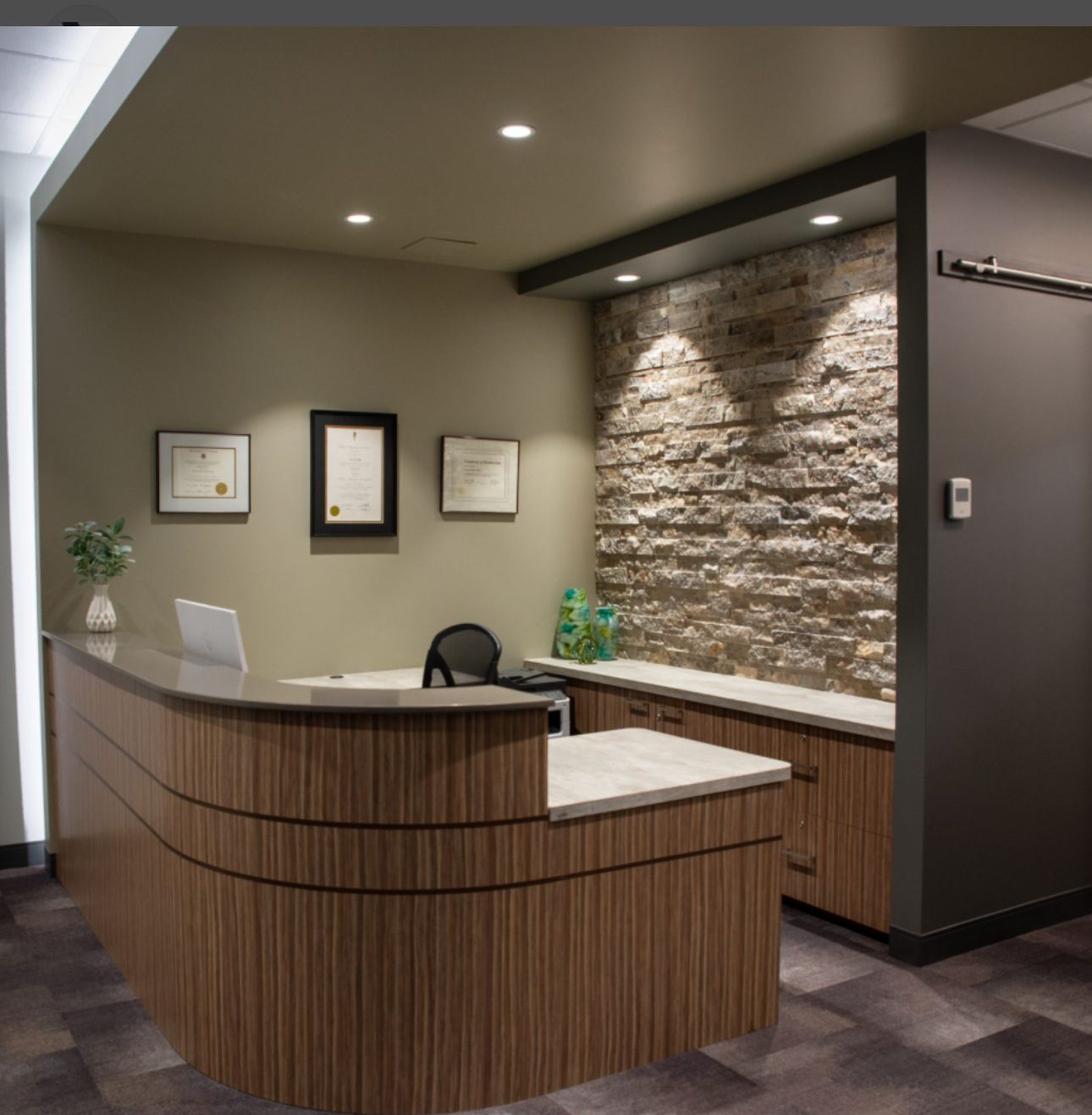 Completed professional office remodel featuring curved wood reception desk stacked stone accent wall and recessed lighting by commercial remodeling contractor serving Marietta GA