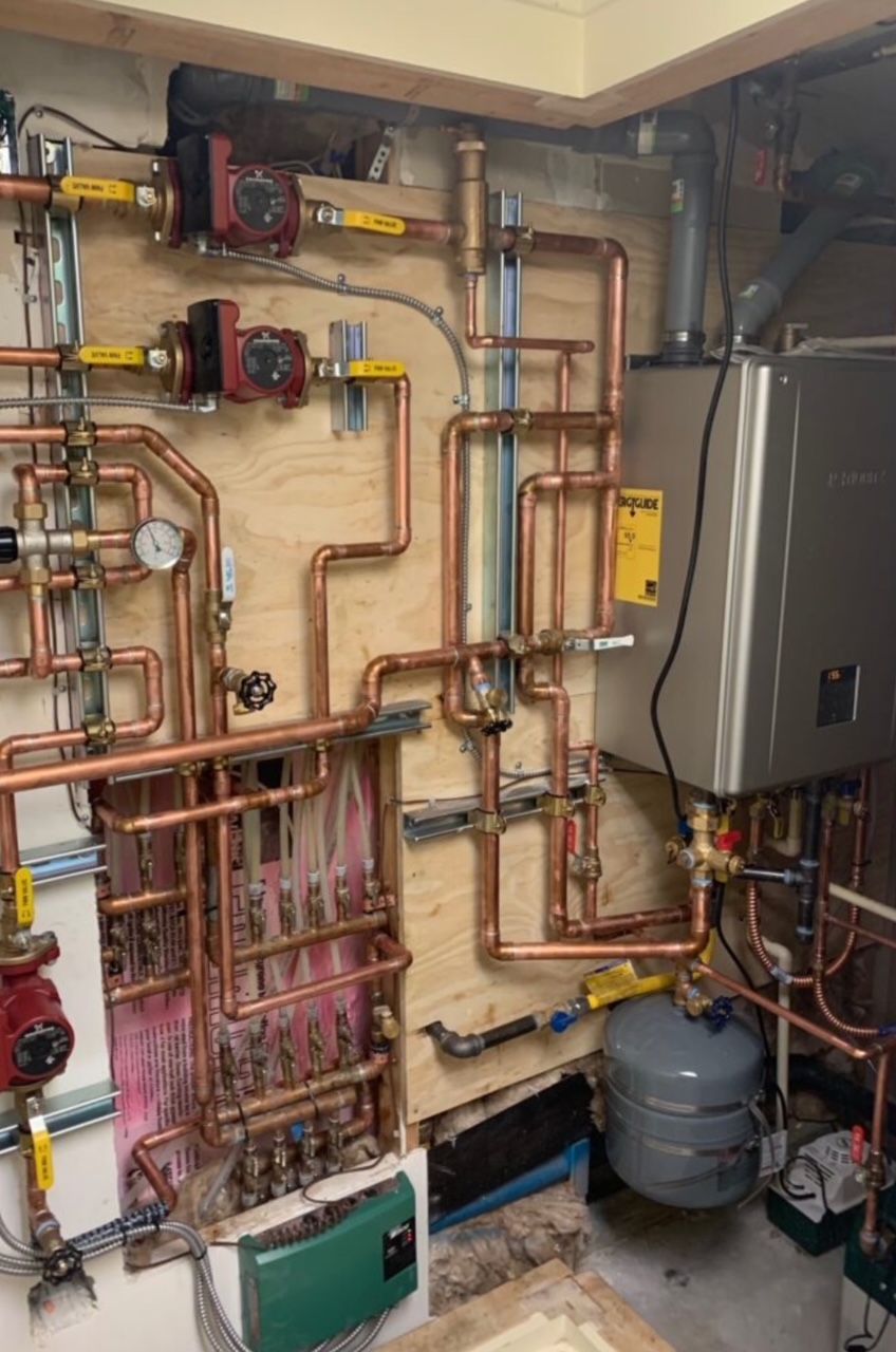 Residential radiant heat mechanical room with copper piping, circulator pumps, and tankless water heater in Marietta Georgia