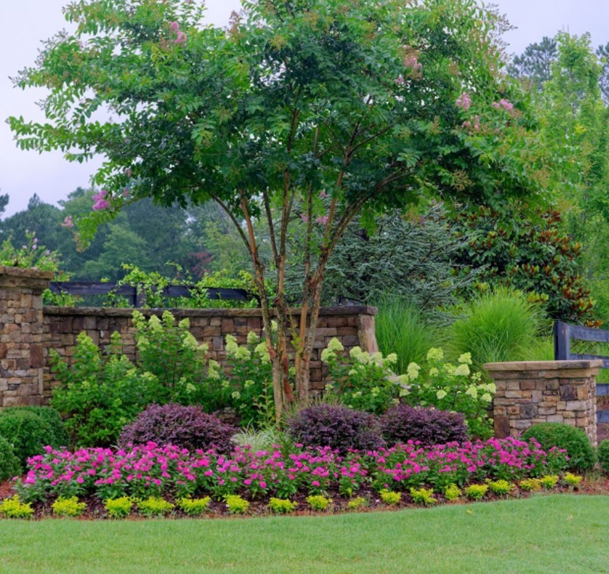 Completed residential stone retaining wall with professional landscaping flower beds and crape myrtle tree by contractor serving Woodstock and Cherokee County GA