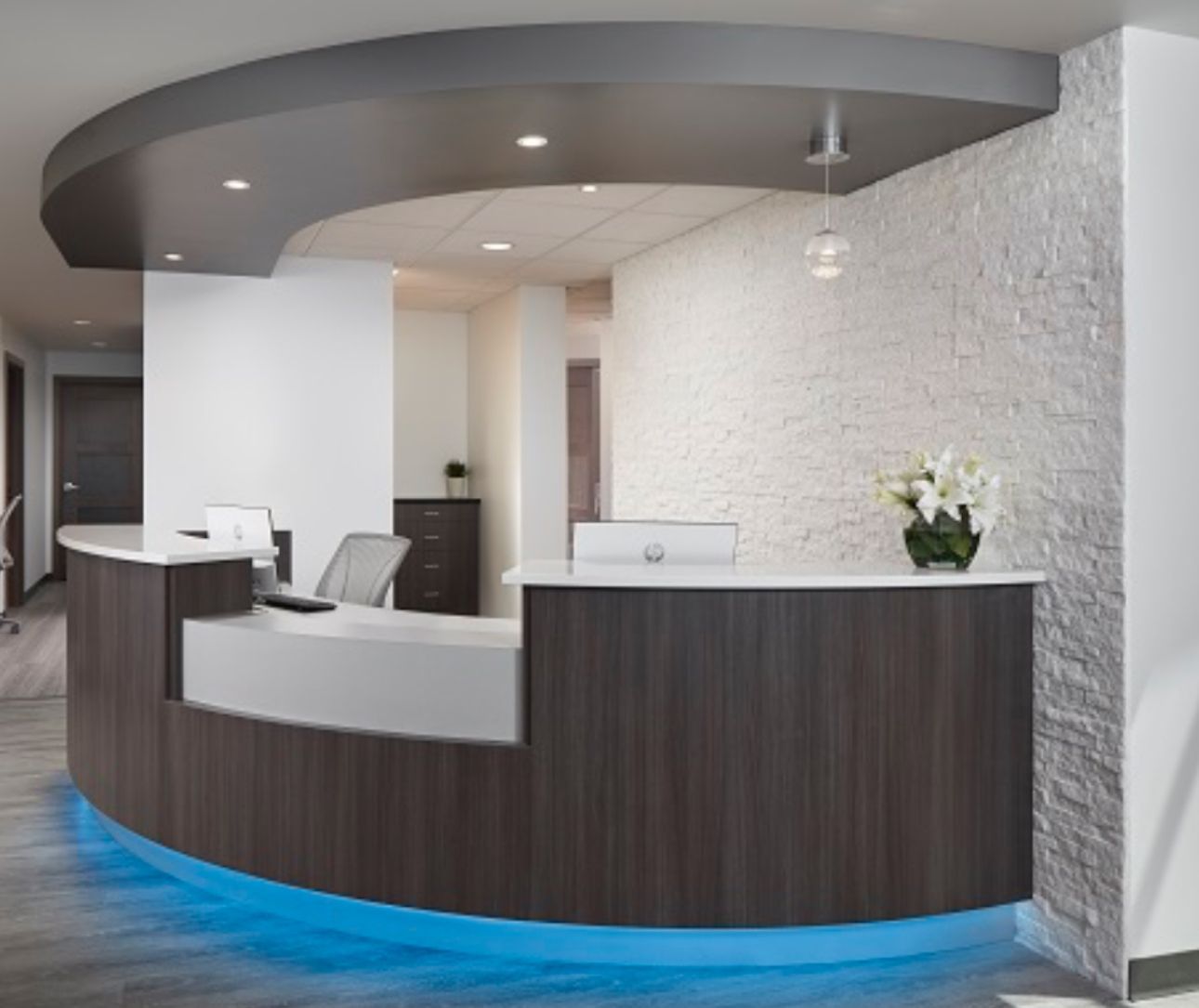 Upscale commercial office interior remodel featuring dark wood curved reception desk LED accent lighting white stacked stone and pendant lighting by contractor serving Woodstock GA