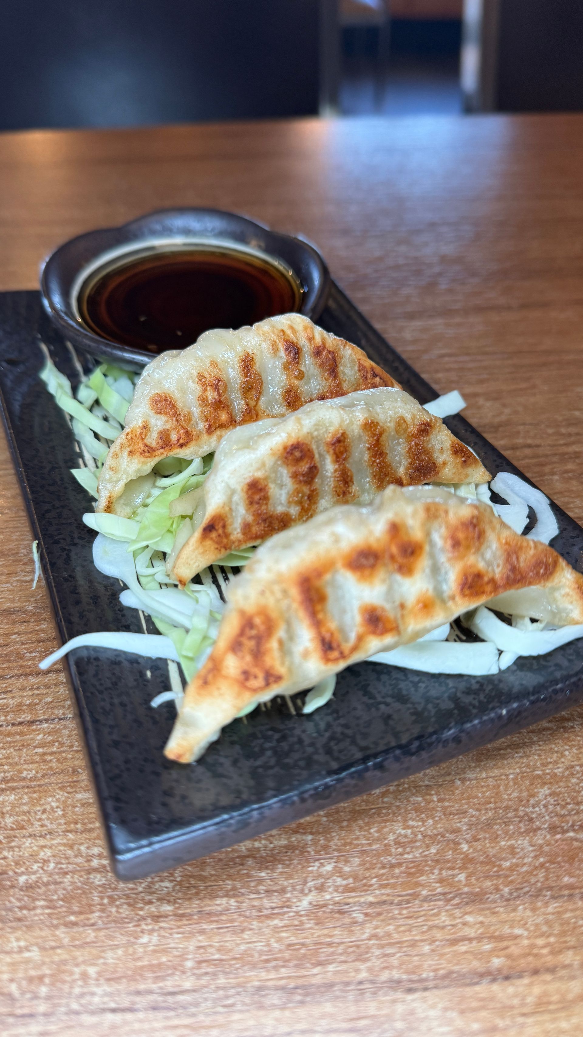 Pan-fried dumplings with dipping sauce on a bed of shredded cabbage, served on a black rectangular plate.