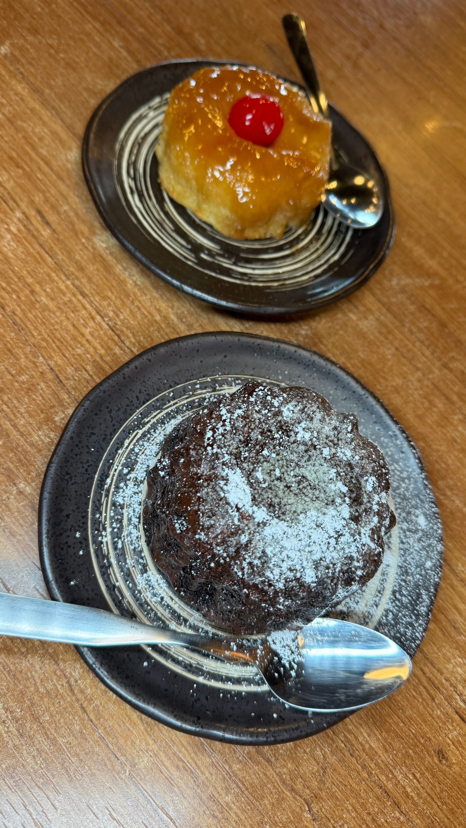 Two desserts on black plates: a pineapple upside-down cake and a chocolate cake dusted with powdered sugar.