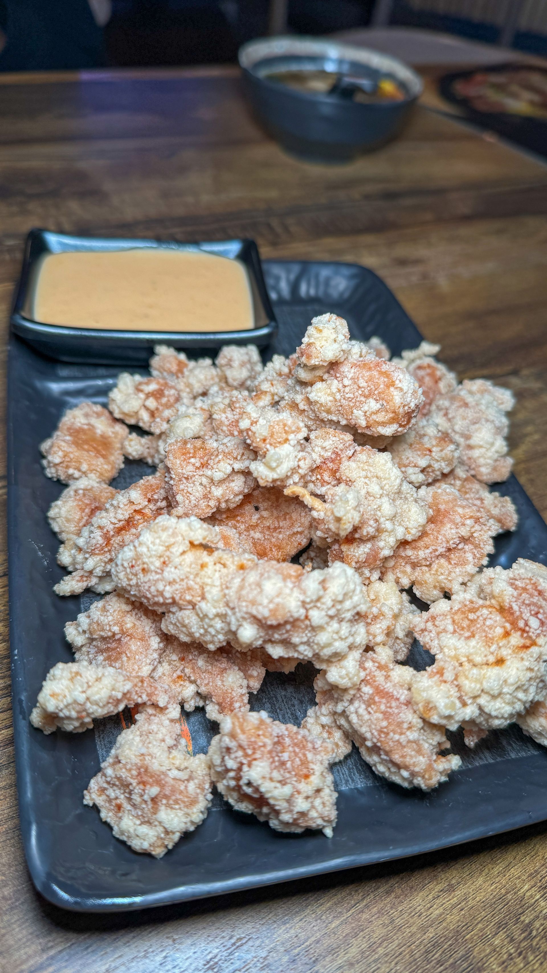 A black plate topped with fried shrimp and dipping sauce on a wooden table.