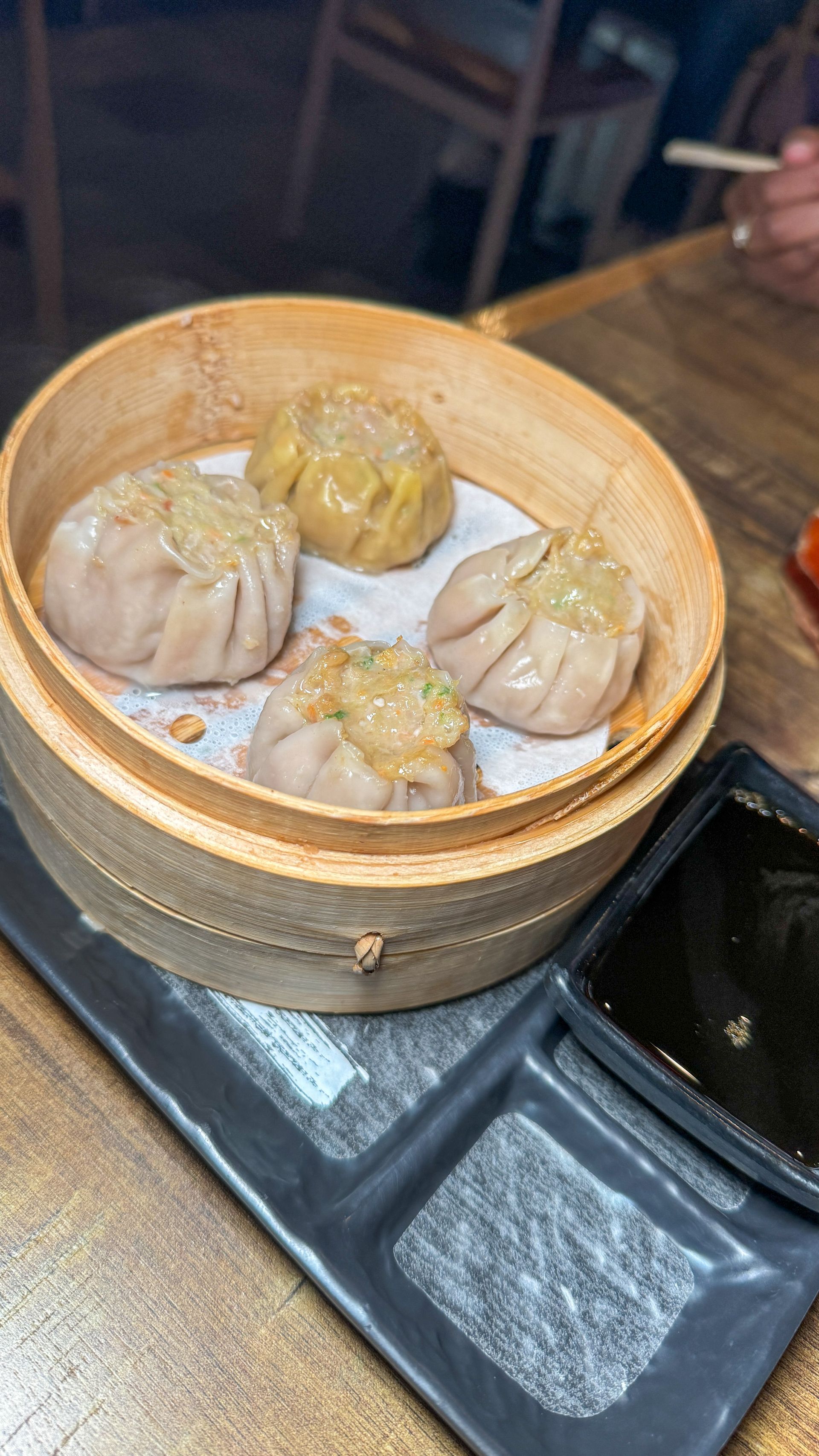 A close up of dim sum in a bamboo steamer on a plate on a table.