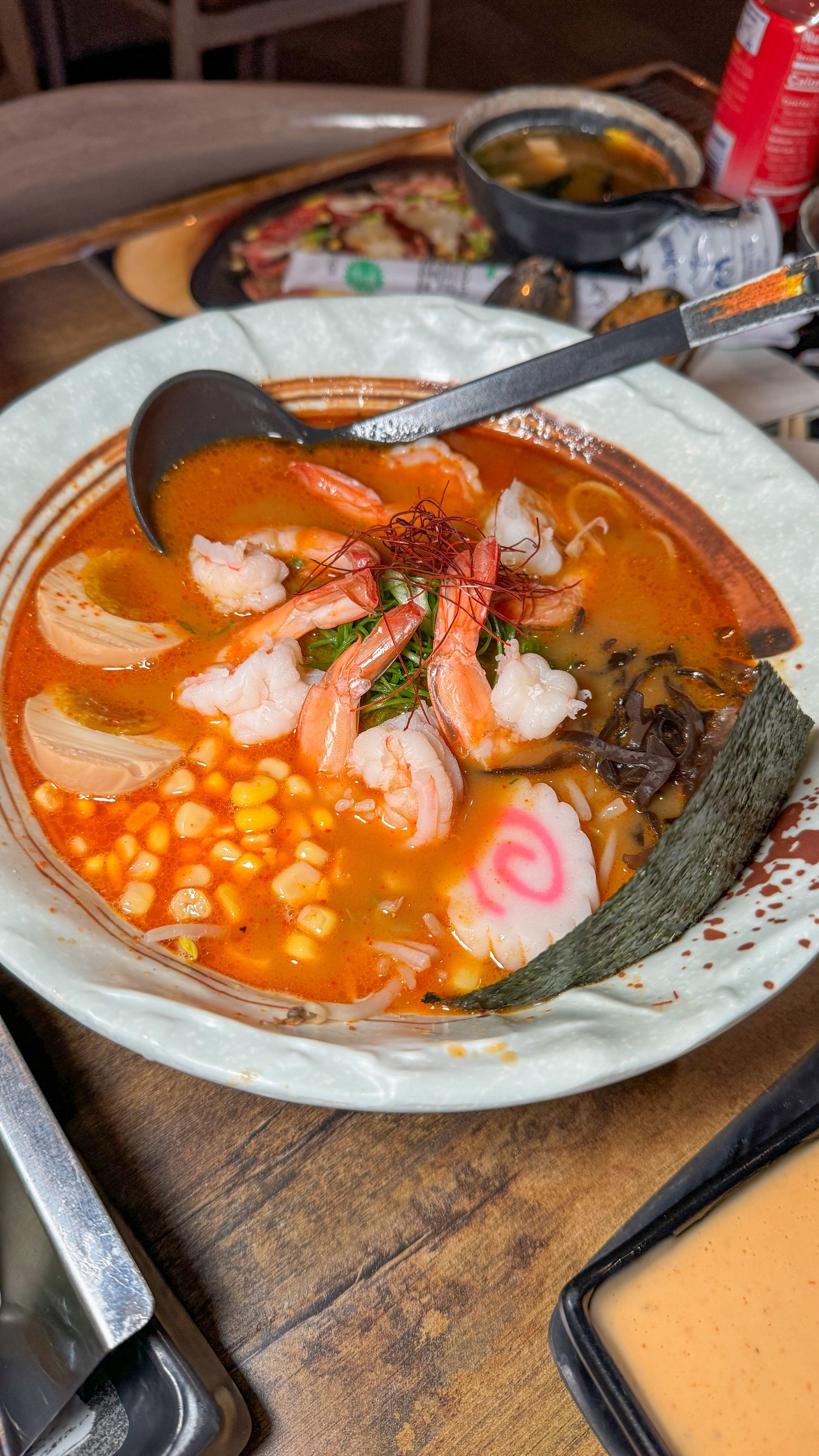 A bowl of ramen with shrimp and corn on a table.