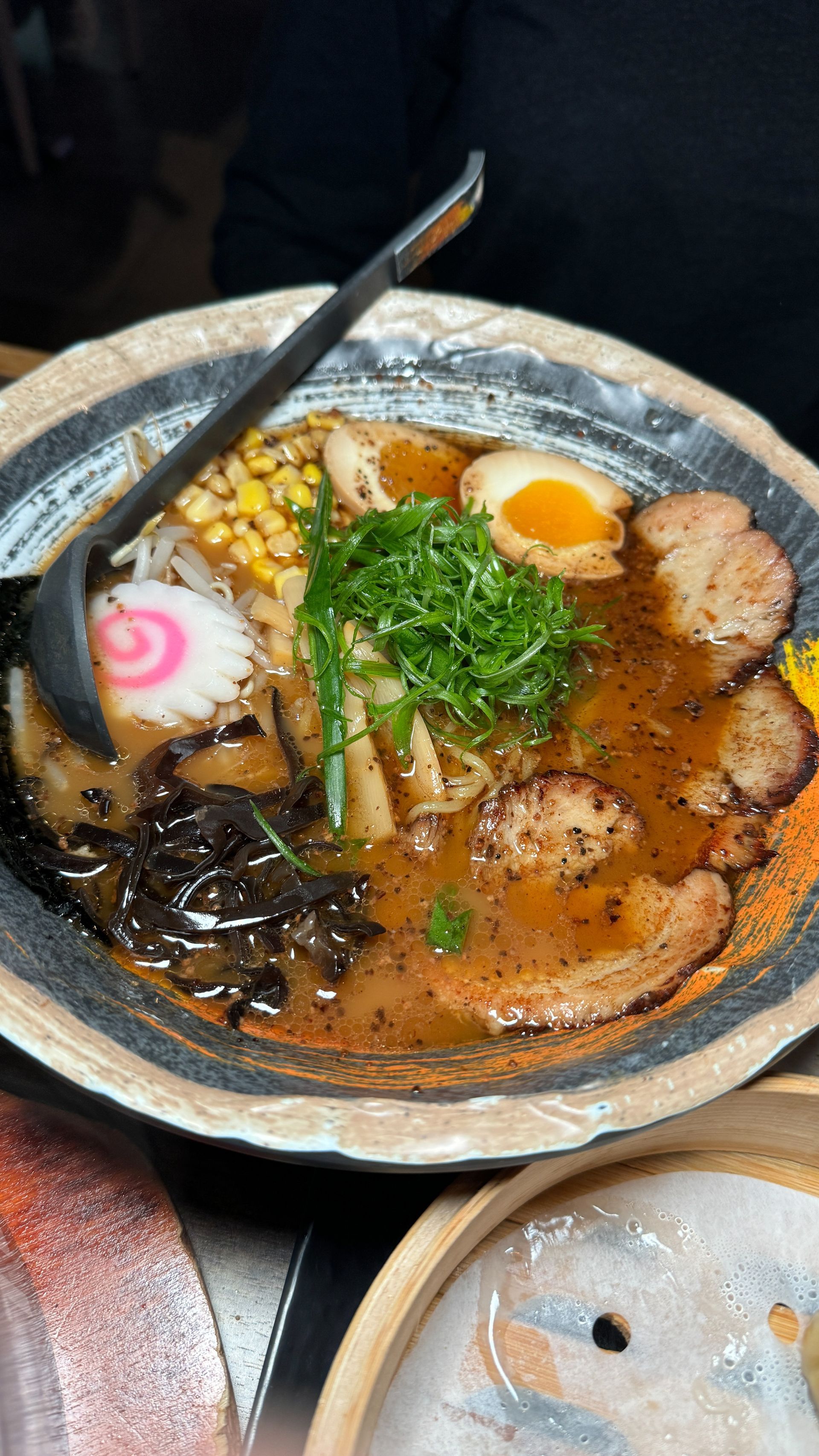 A bowl of ramen with a ladle in it on a table.