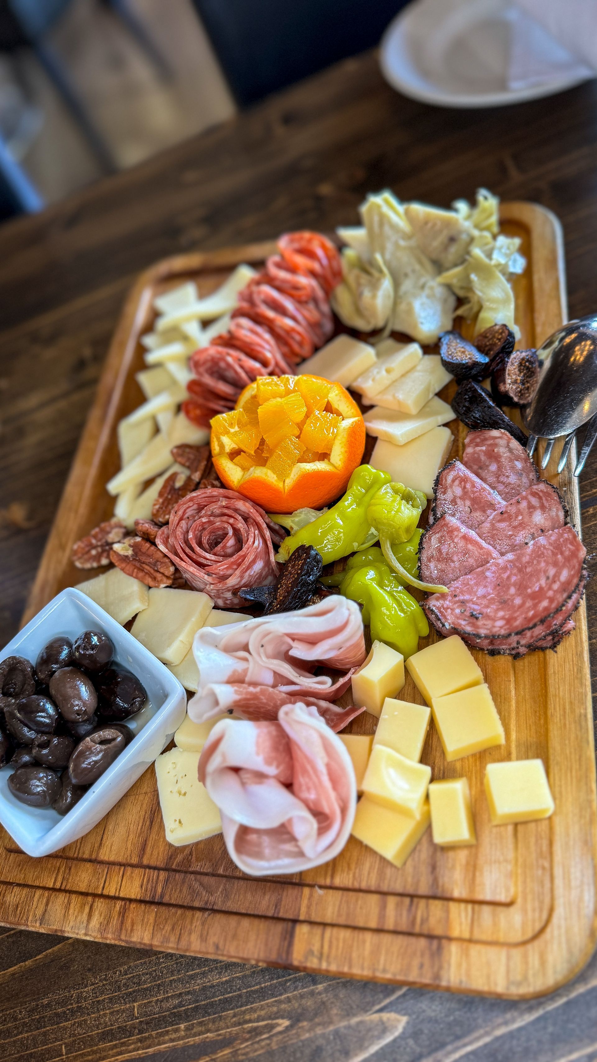 Charcuterie board: meats, cheeses, olives, pepperoncini, and artichoke hearts on wooden board.