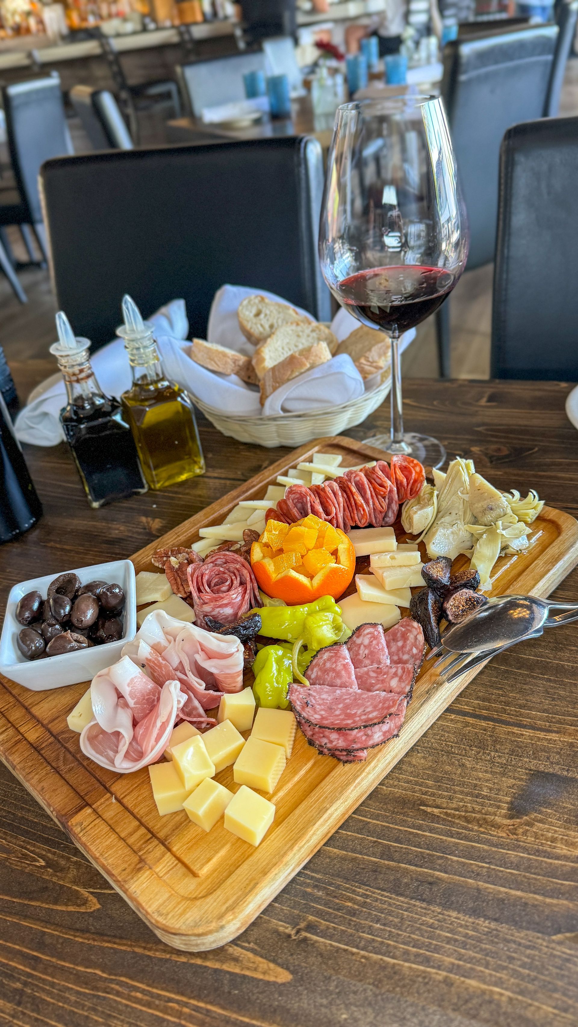 Charcuterie board with meats, cheeses, olives, and bread, alongside wine and olive oil.