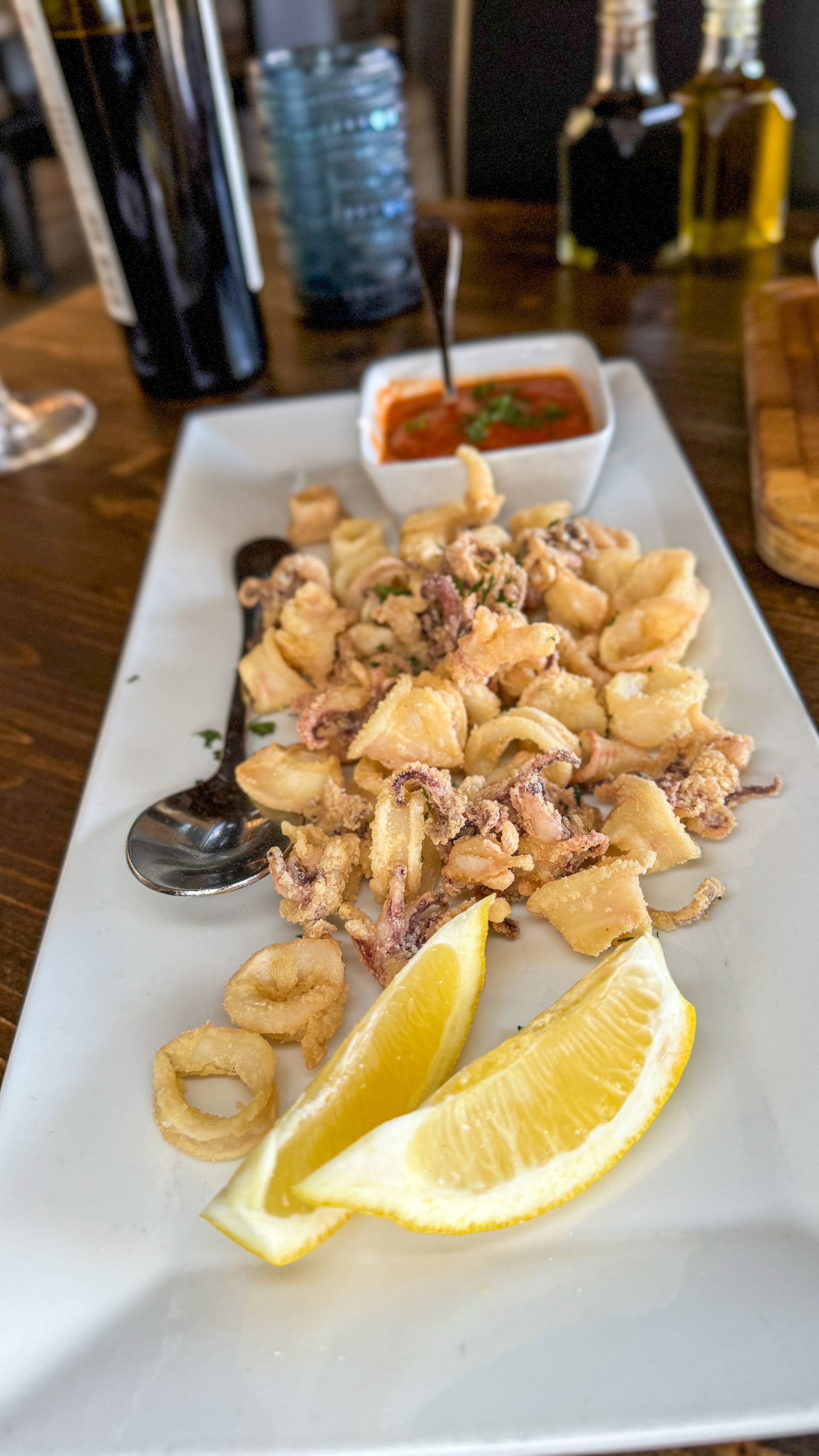 Fried calamari with marinara sauce and lemon wedges on a white plate.