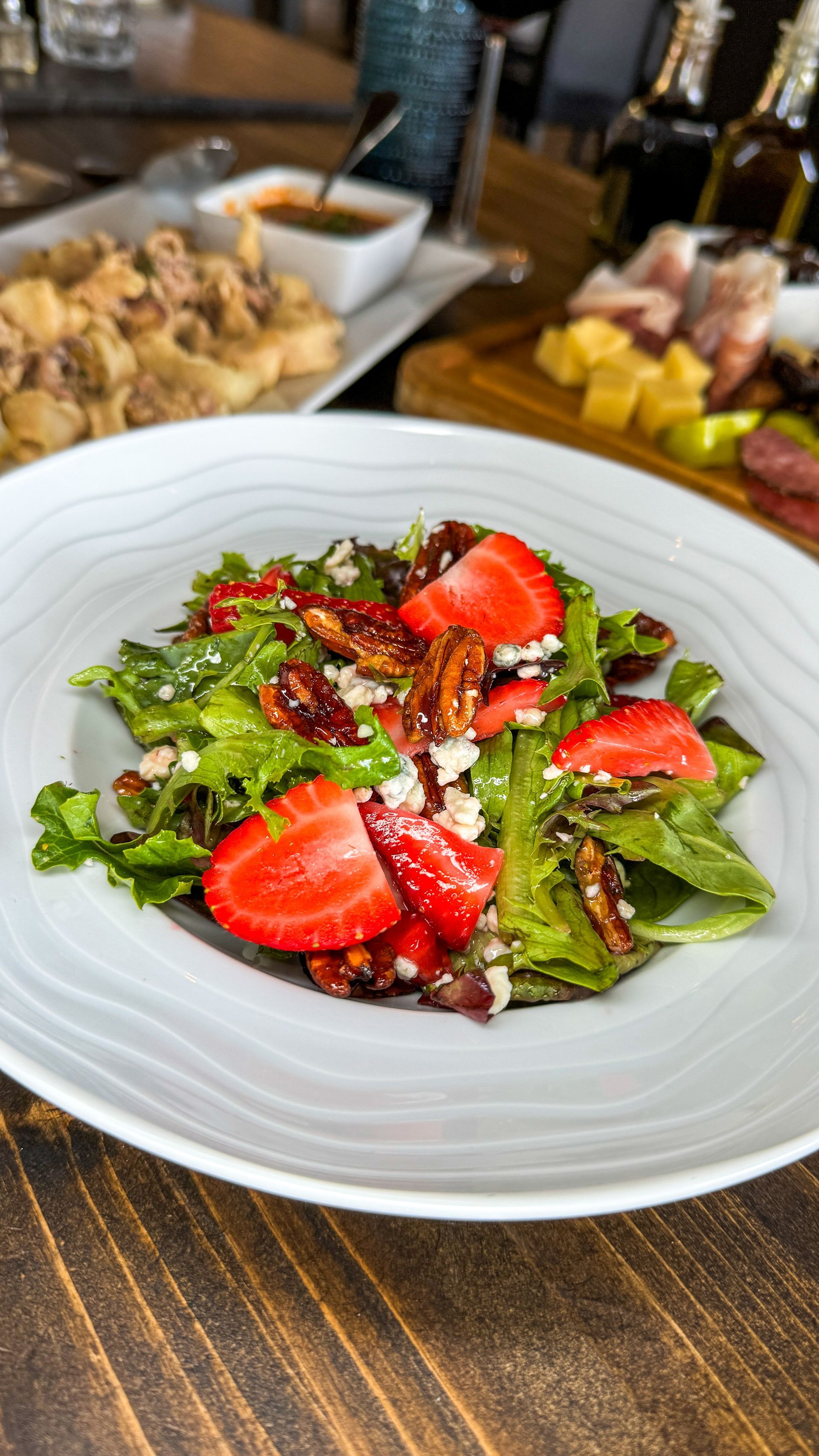 Strawberry salad with pecans and cheese in a white bowl, other dishes in the background.