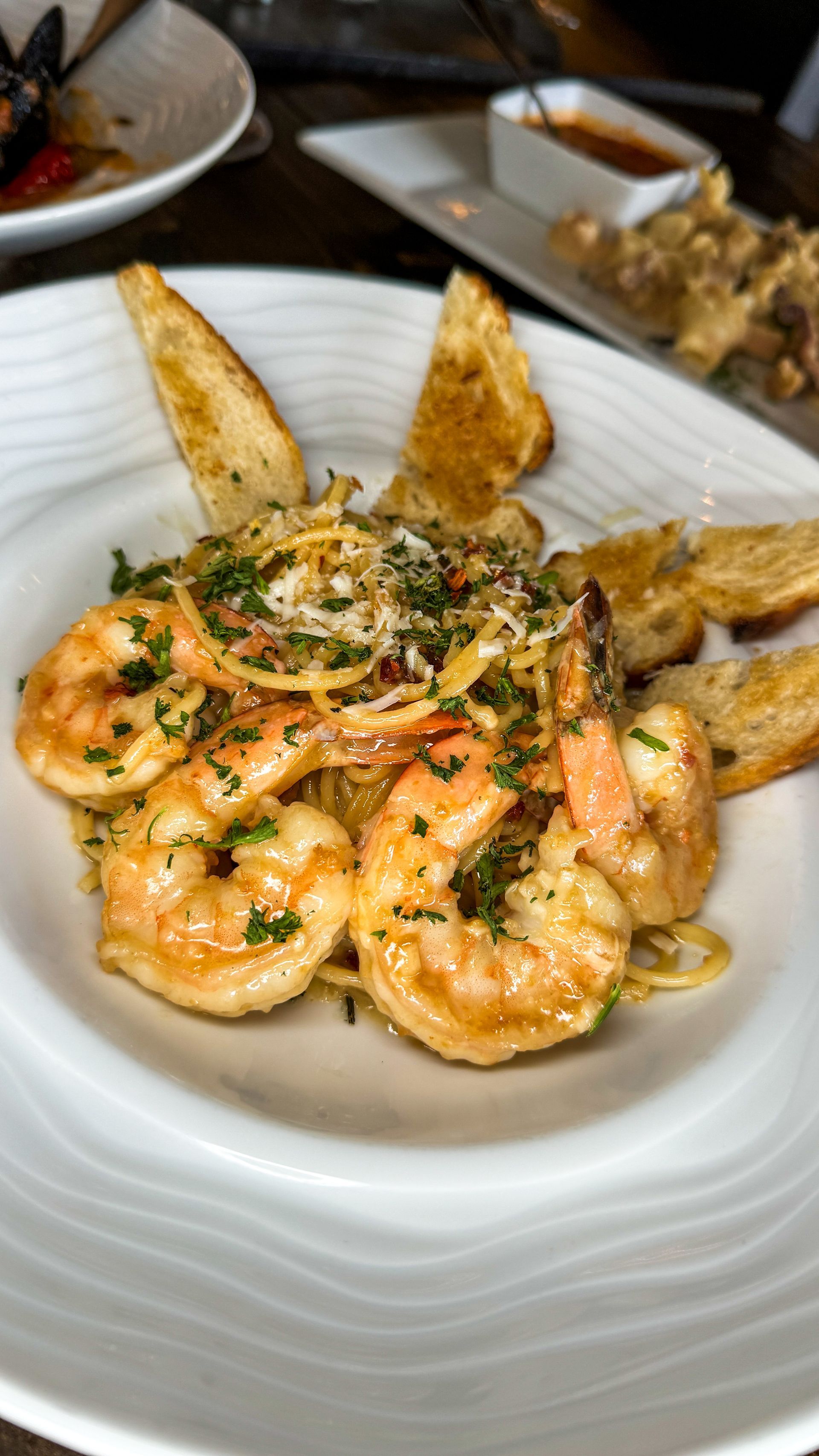 Shrimp scampi in a white bowl, garnished with herbs and served with toasted bread.