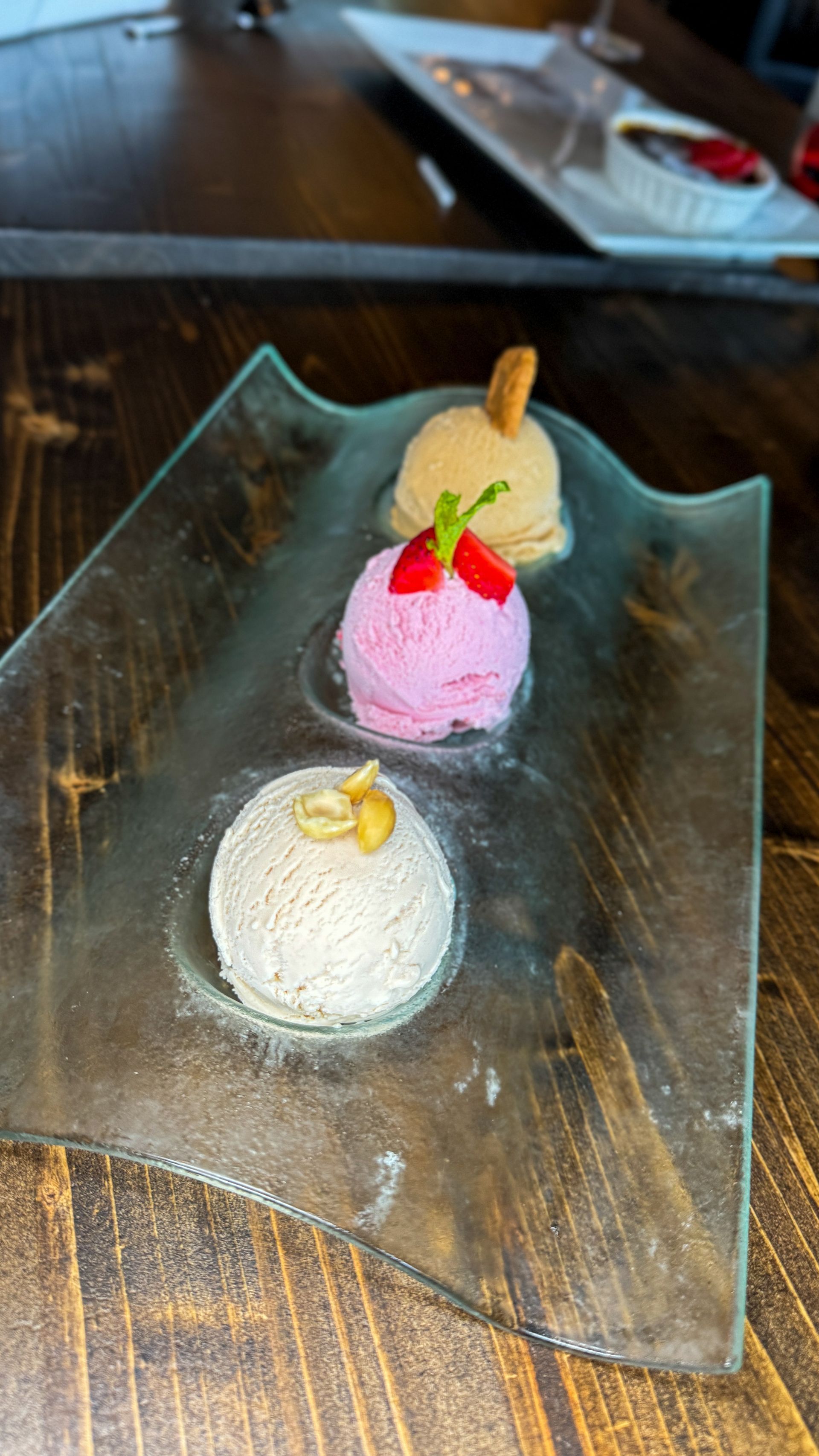 Three scoops of ice cream on a clear, angular plate. Flavors: light brown, pink, and white. 