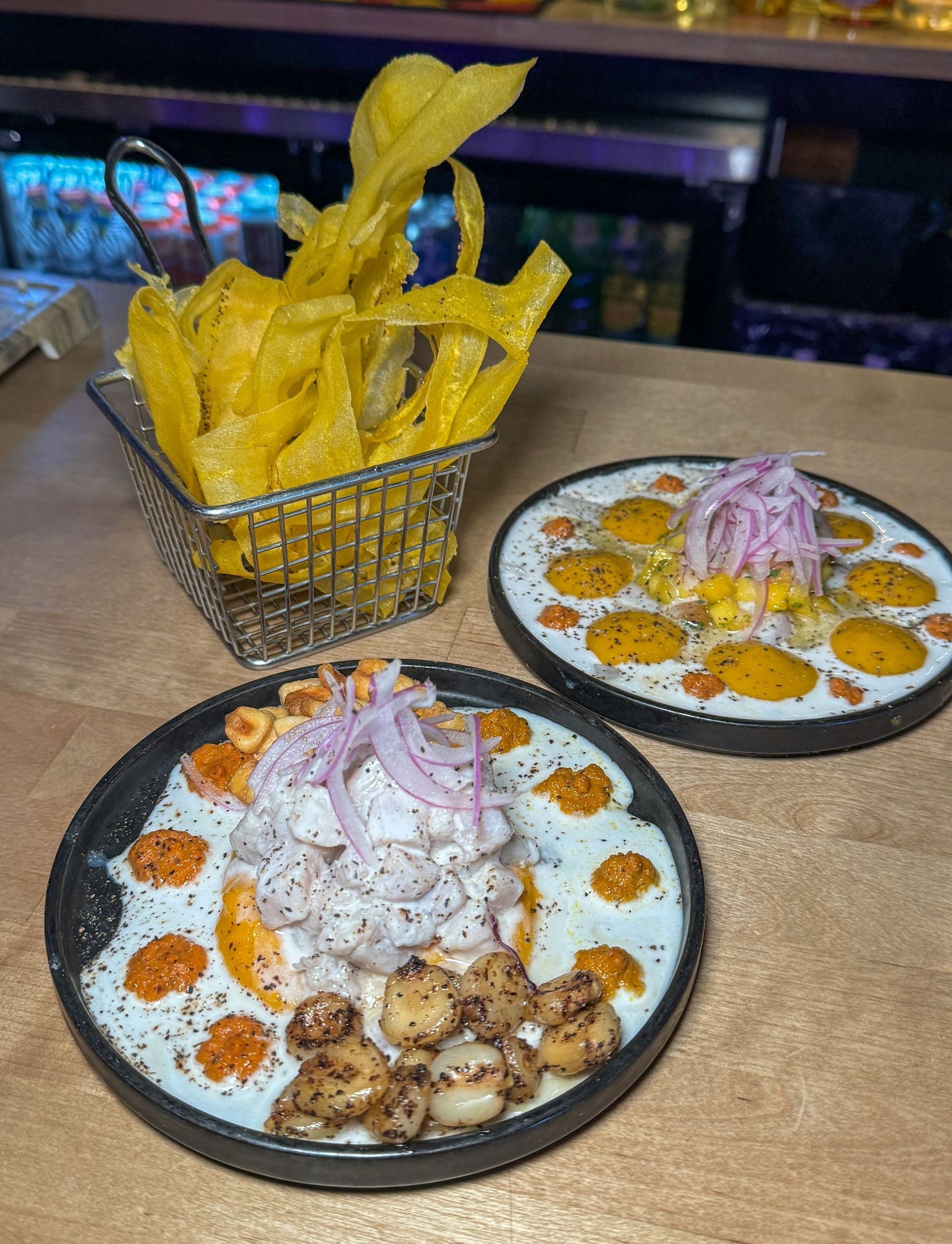 Two plates of food are on a table next to a basket of chips.