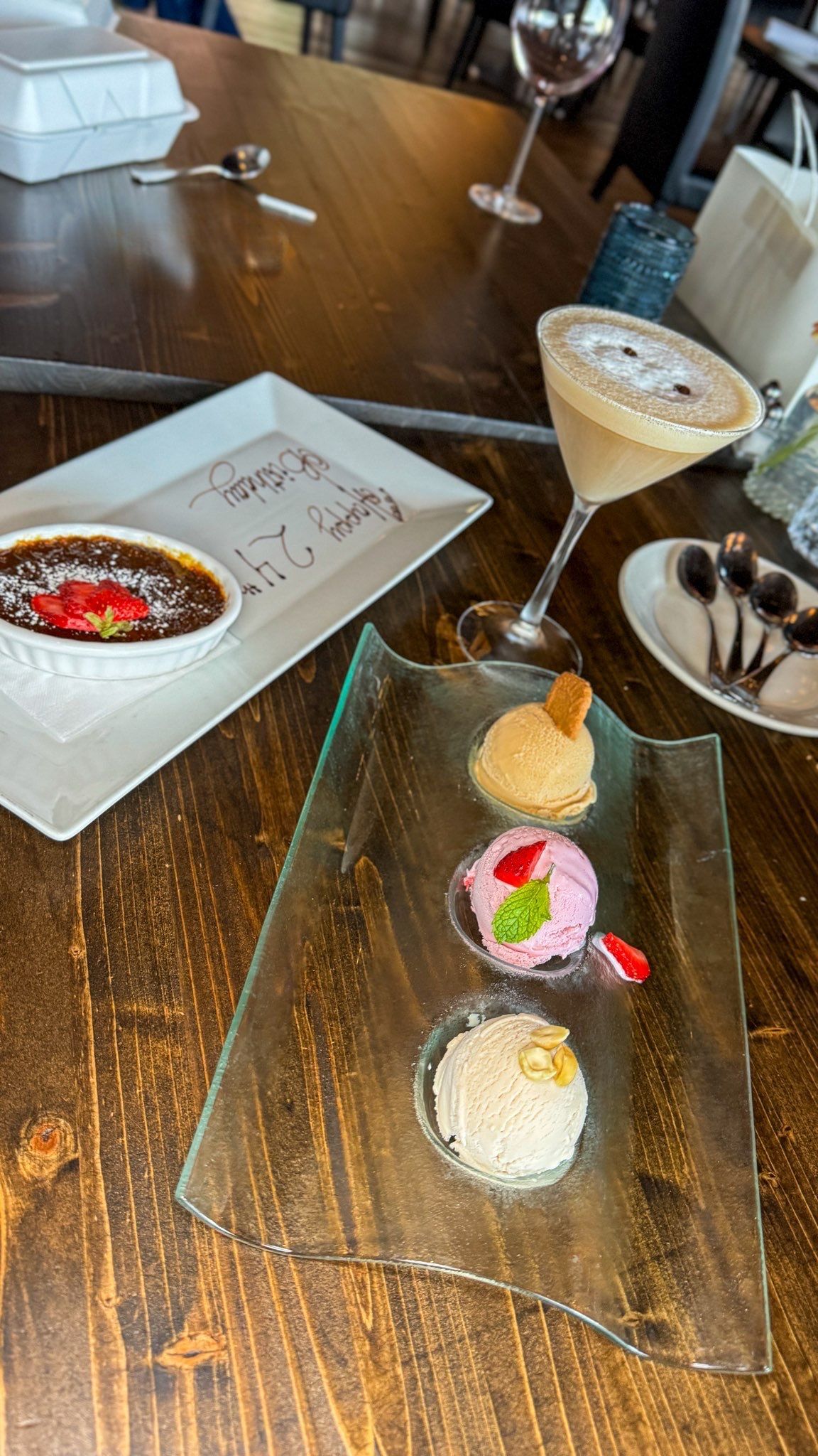 Desserts on a wooden table. Creme brûlée, ice cream trio, cocktail, and spoons.