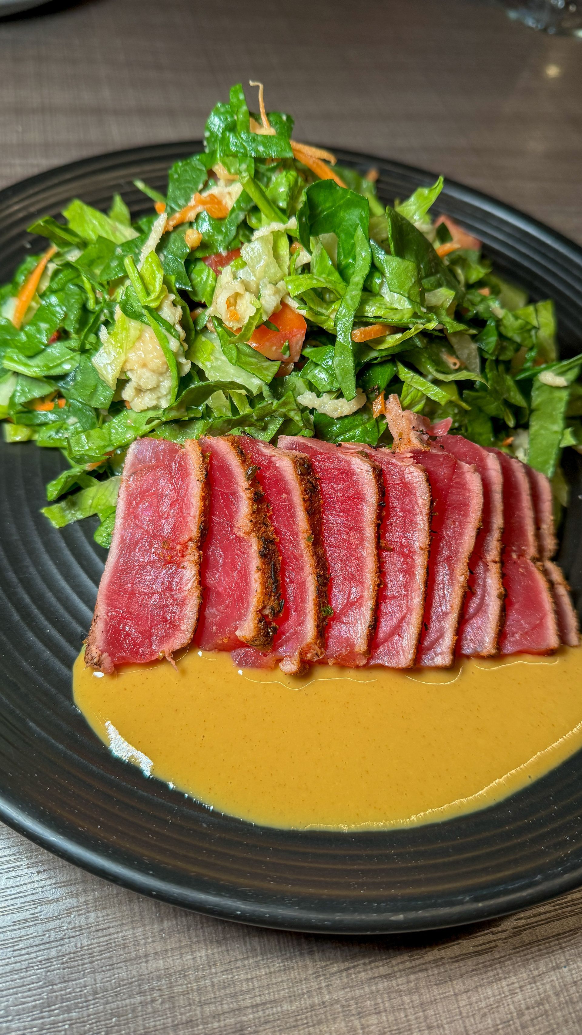 A black plate topped with sliced meat and a salad on a table.